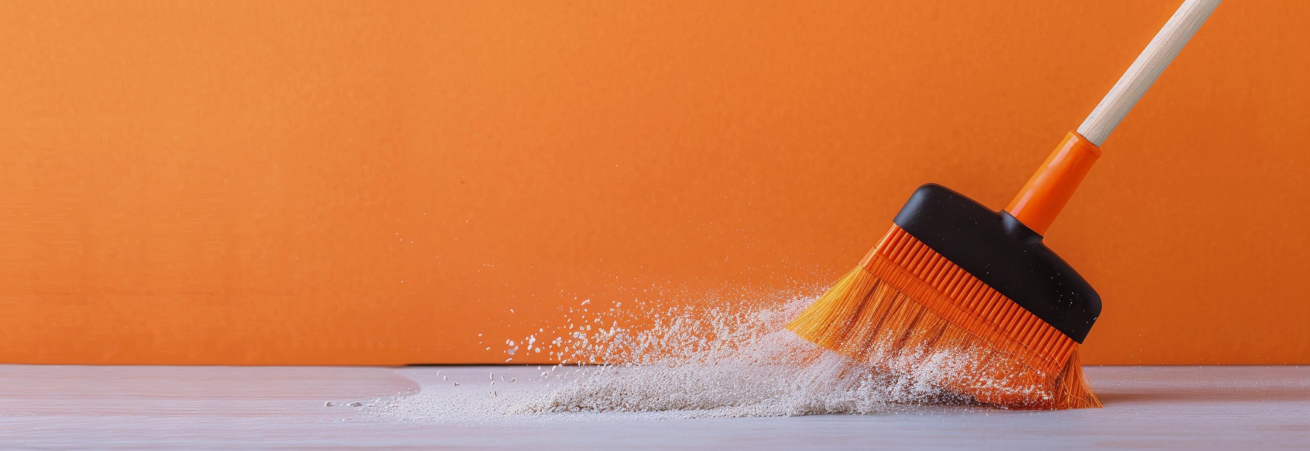 Broom Sweeping Dust on Wooden Surface With Orange Background Stock Free