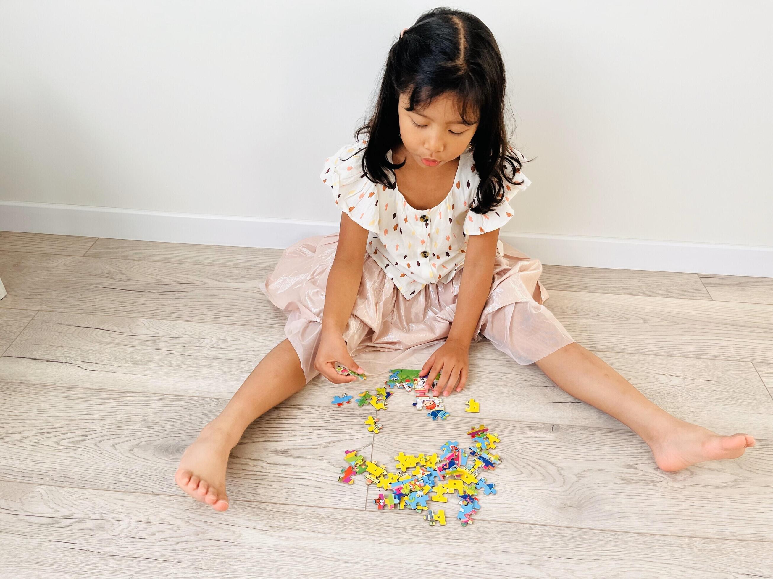 A five year old Asian girl is sitting on the floor with a wooden motif playing with jigsaw puzzle Stock Free