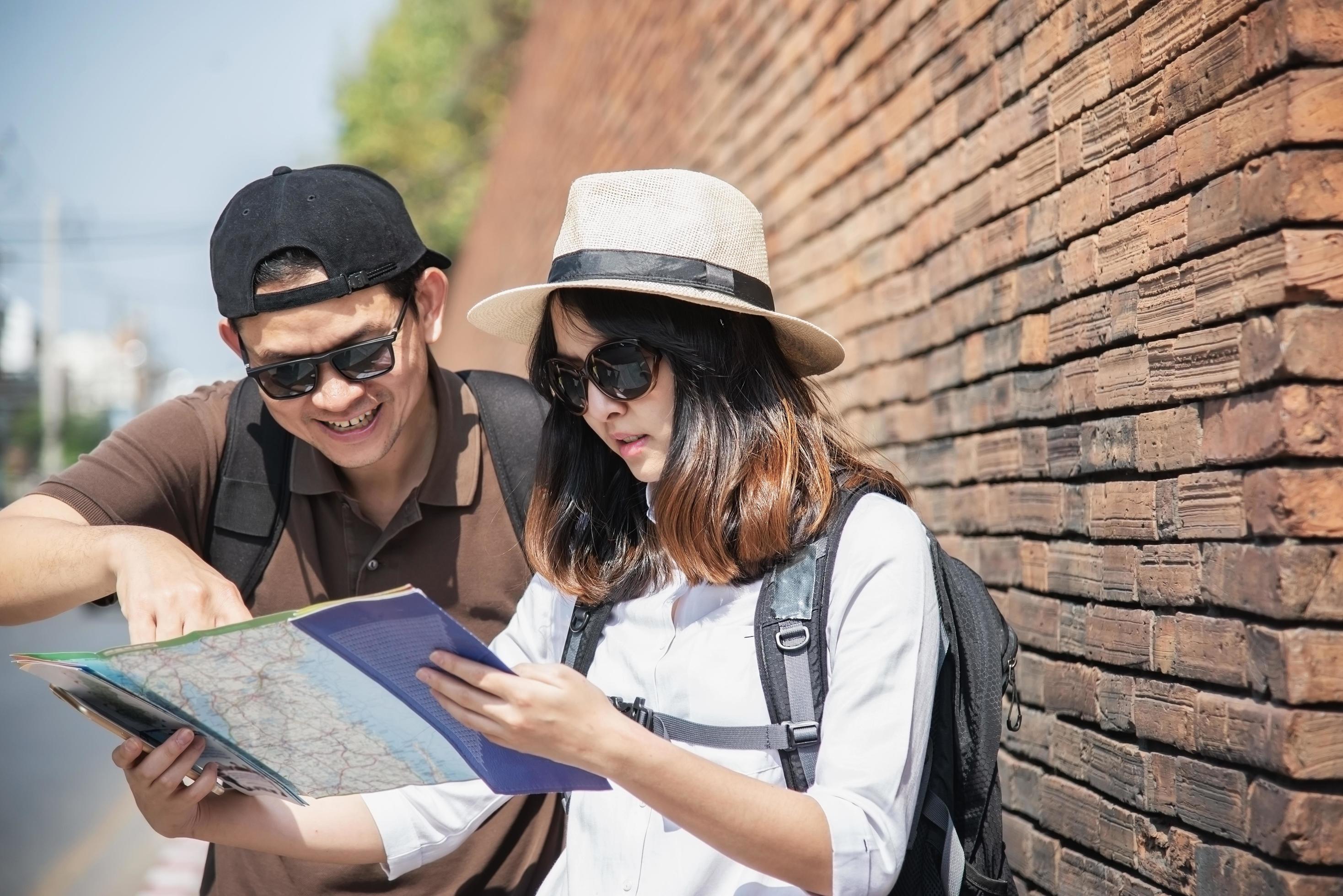 Asian backpack couple tourist holding city map crossing the road – travel people vacation lifestyle concept Stock Free