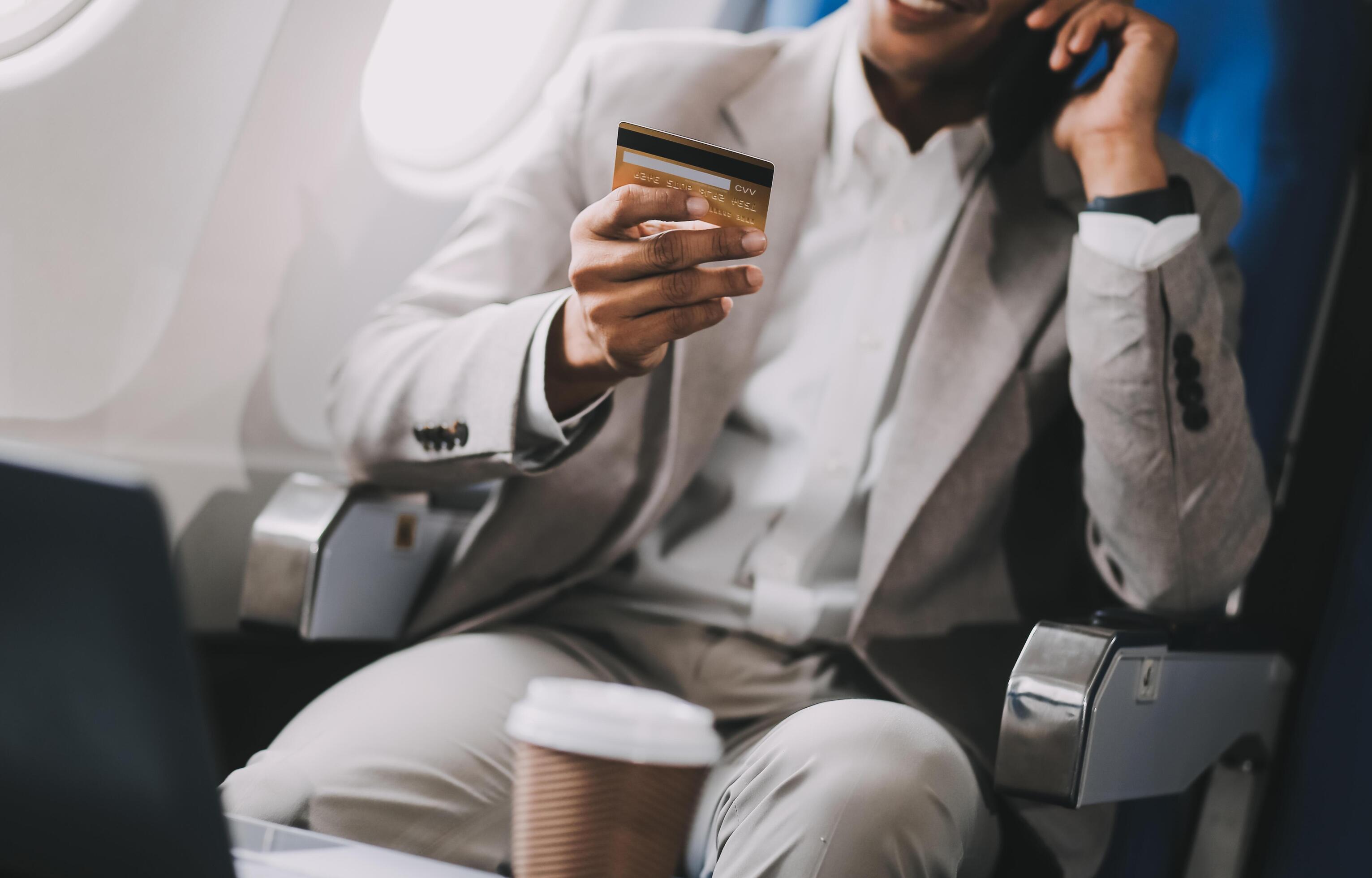 Businessman holding credit card and looking at camera near laptop in private jet Stock Free