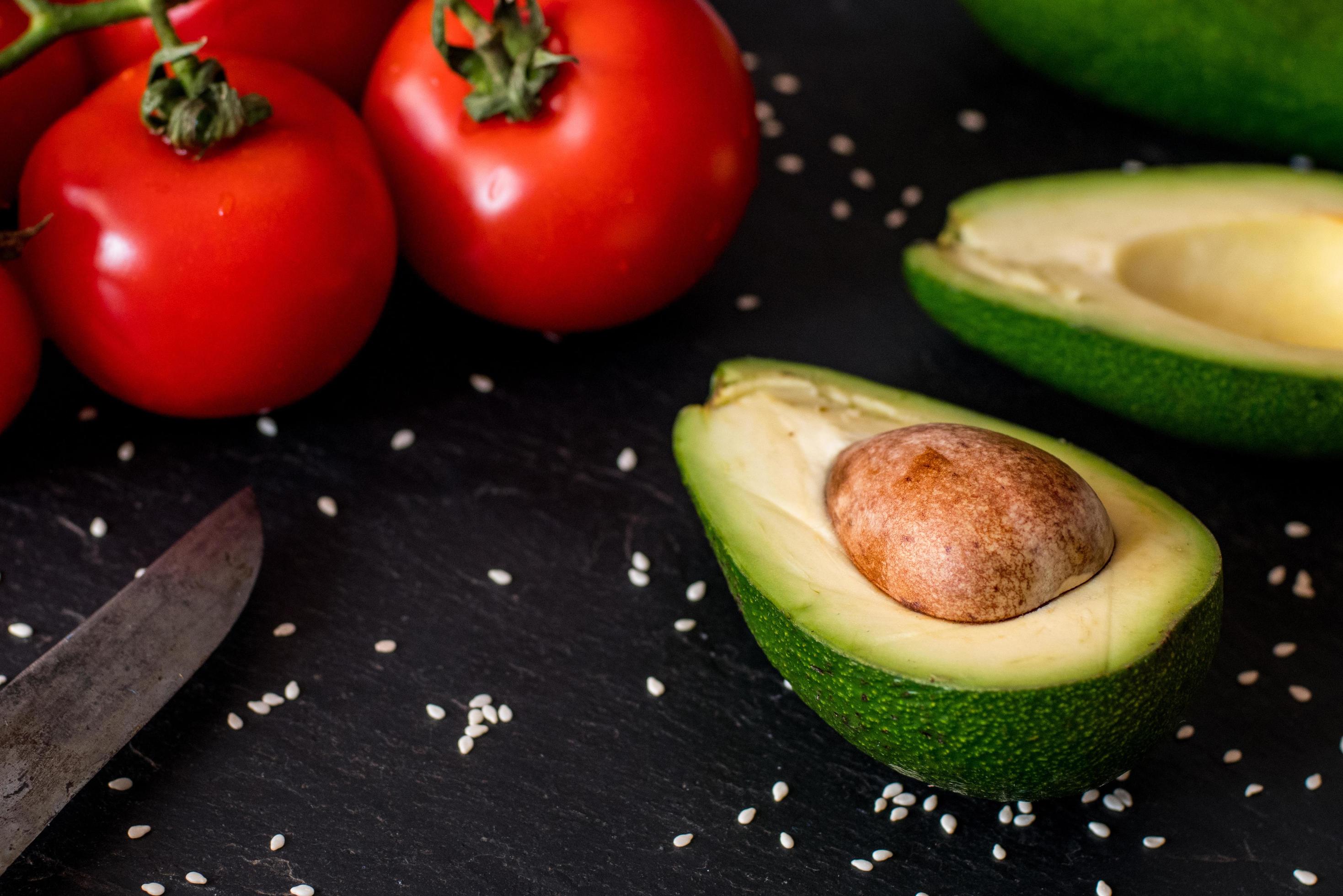 Tomatos and avocado on black table close up, colorful healthy food Stock Free