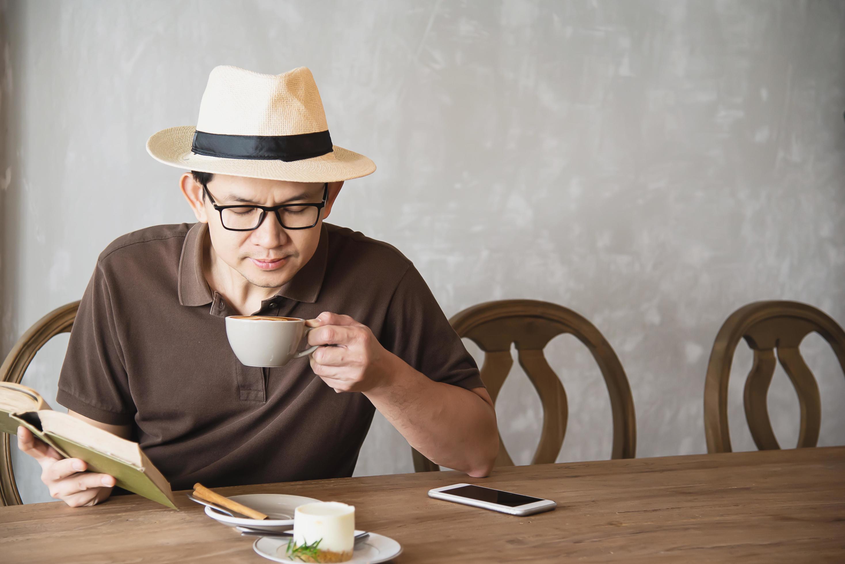 Relax Asian man drink coffee and read book in a modern style coffee shop – people with coffee cup easy lifestyle concept Stock Free