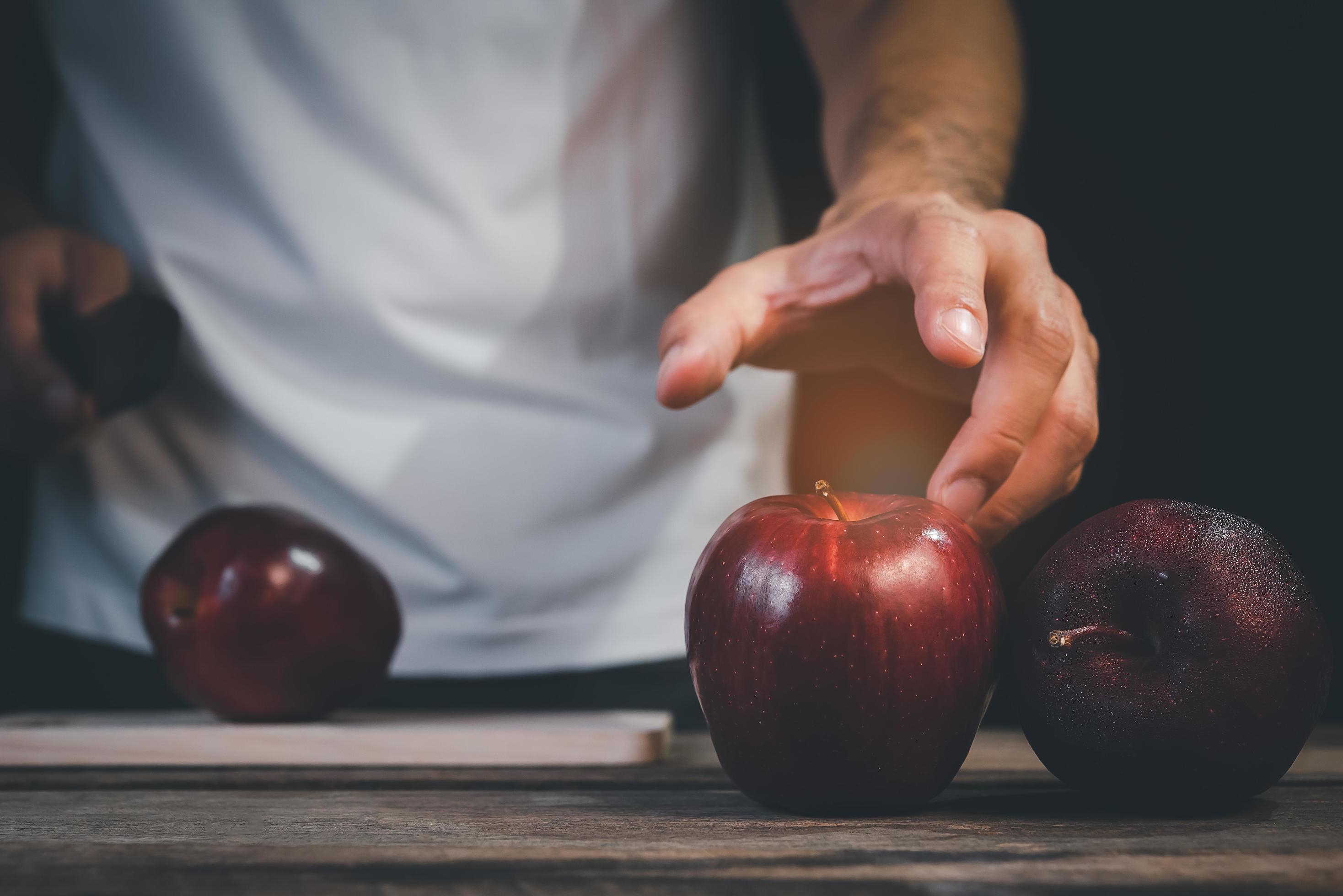 Man hand holding knife prepare to cut red apple on wood table and dark background. Fruits and food concept. Stock Free