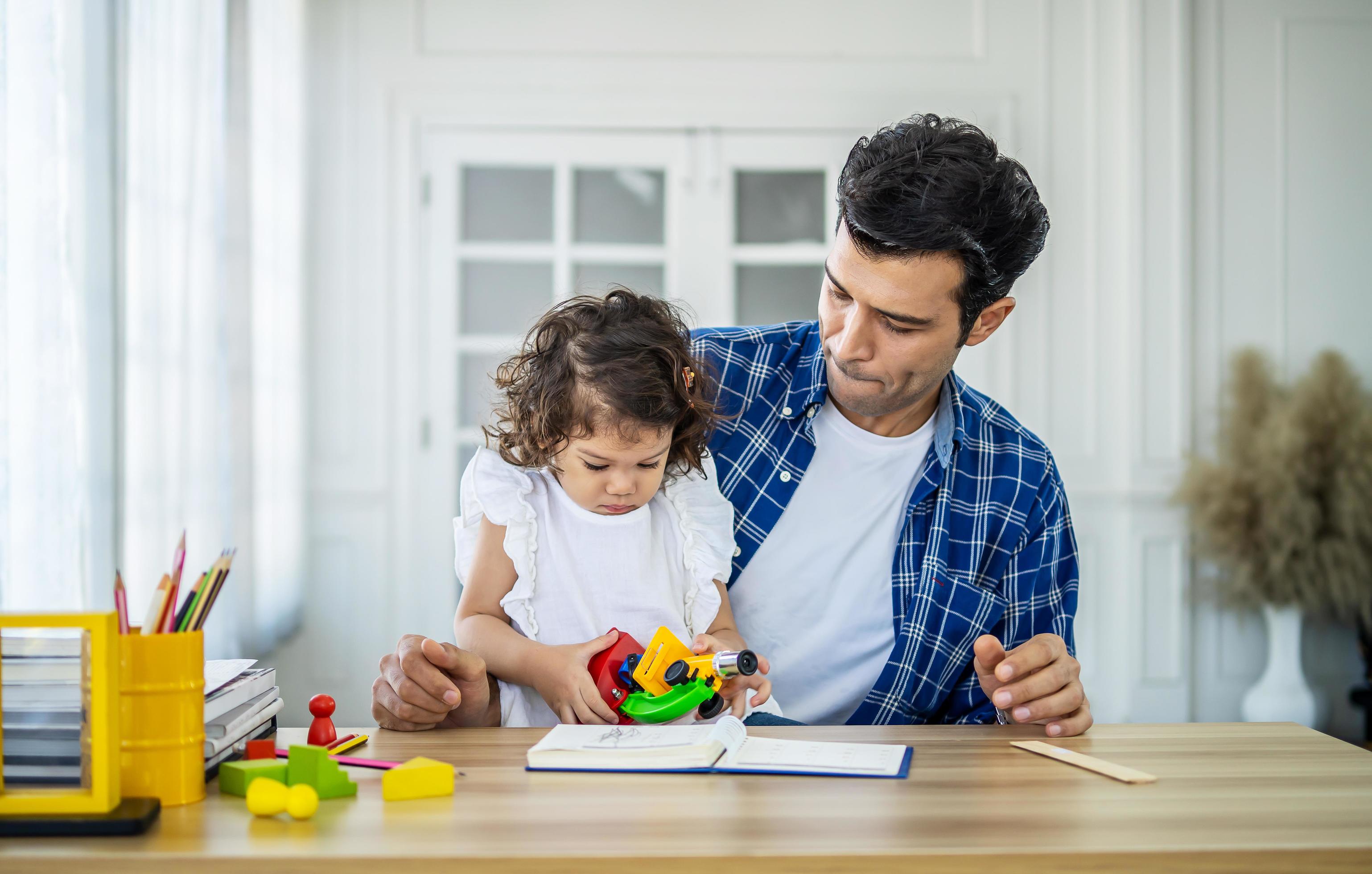 family, fatherhood and childhood concept – happy father and little daughter playing with toy microscope at table at home Stock Free