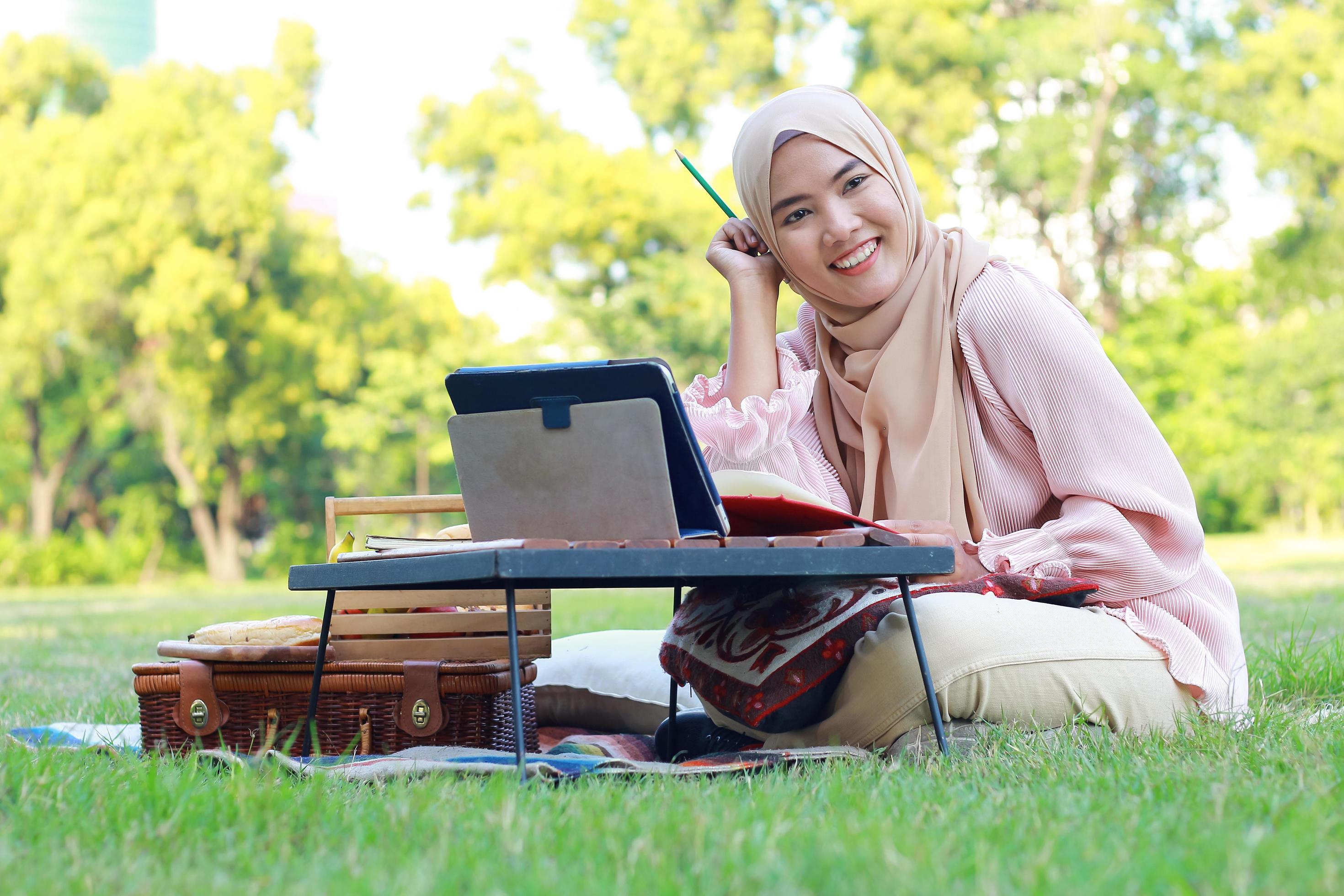 Beautiful Muslim girl sitting happily in the park. Muslim woman smiling in garden lawn. Lifestyle concept of a confident modern woman Stock Free