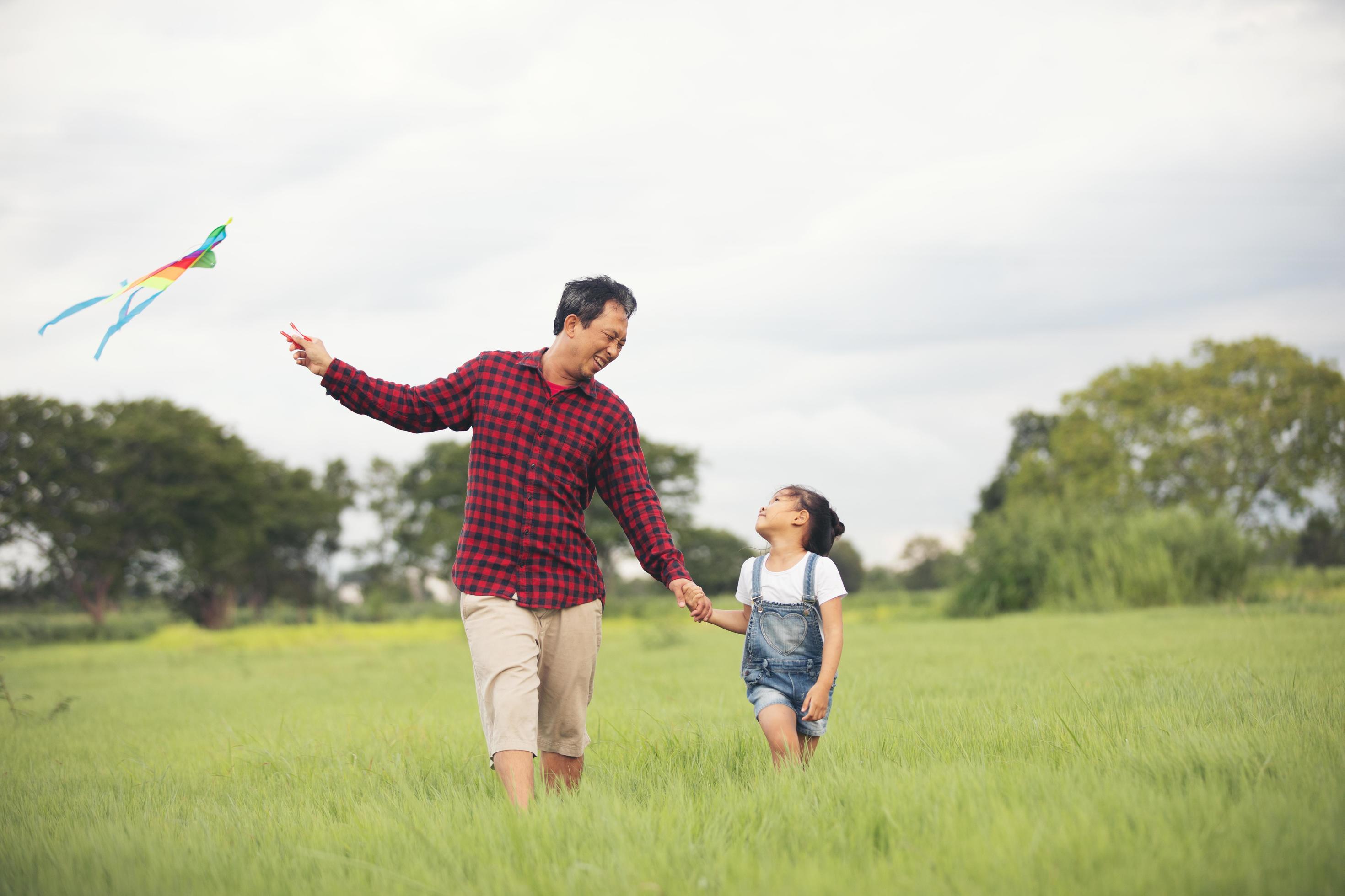 Asian child girl and father with a kite running and happy on meadow in summer in nature Stock Free