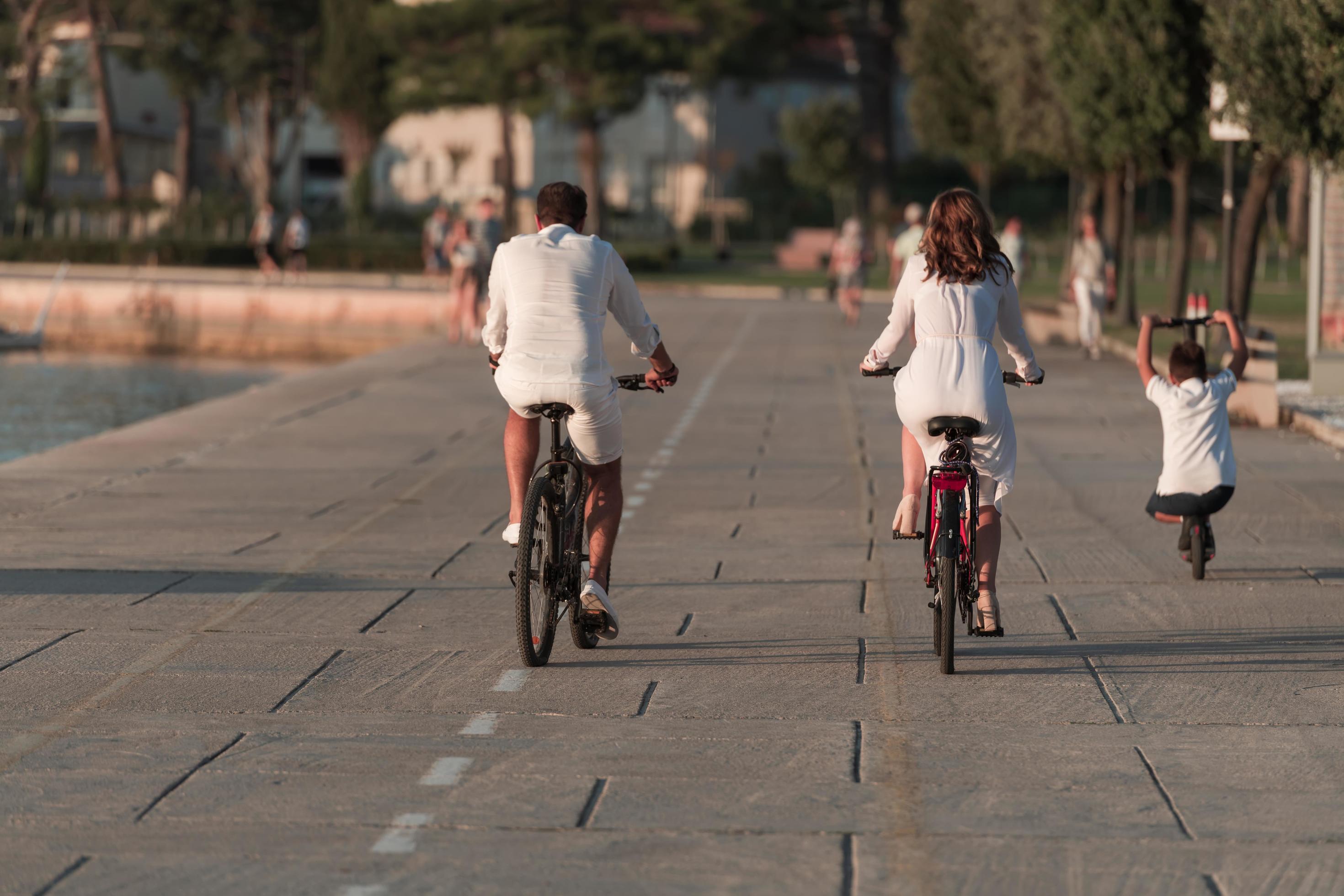 Happy family enjoying a beautiful morning by the sea together, parents riding a bike and their son riding an electric scooter. Selective focus Stock Free