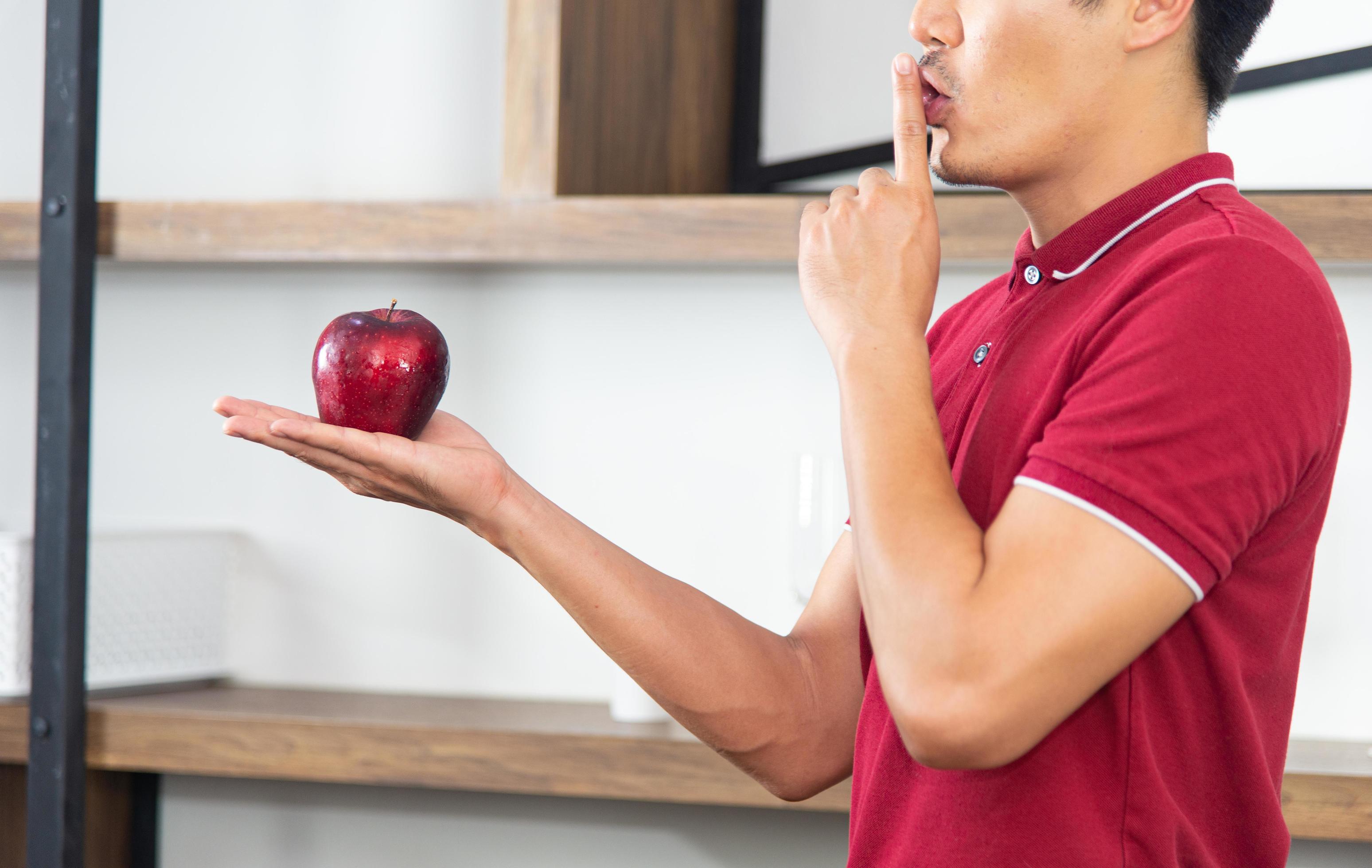 Healthy lifestyle and freshness concept. Smart, young and healthy Asian man eating apple in the loft style kitchen room. Stock Free