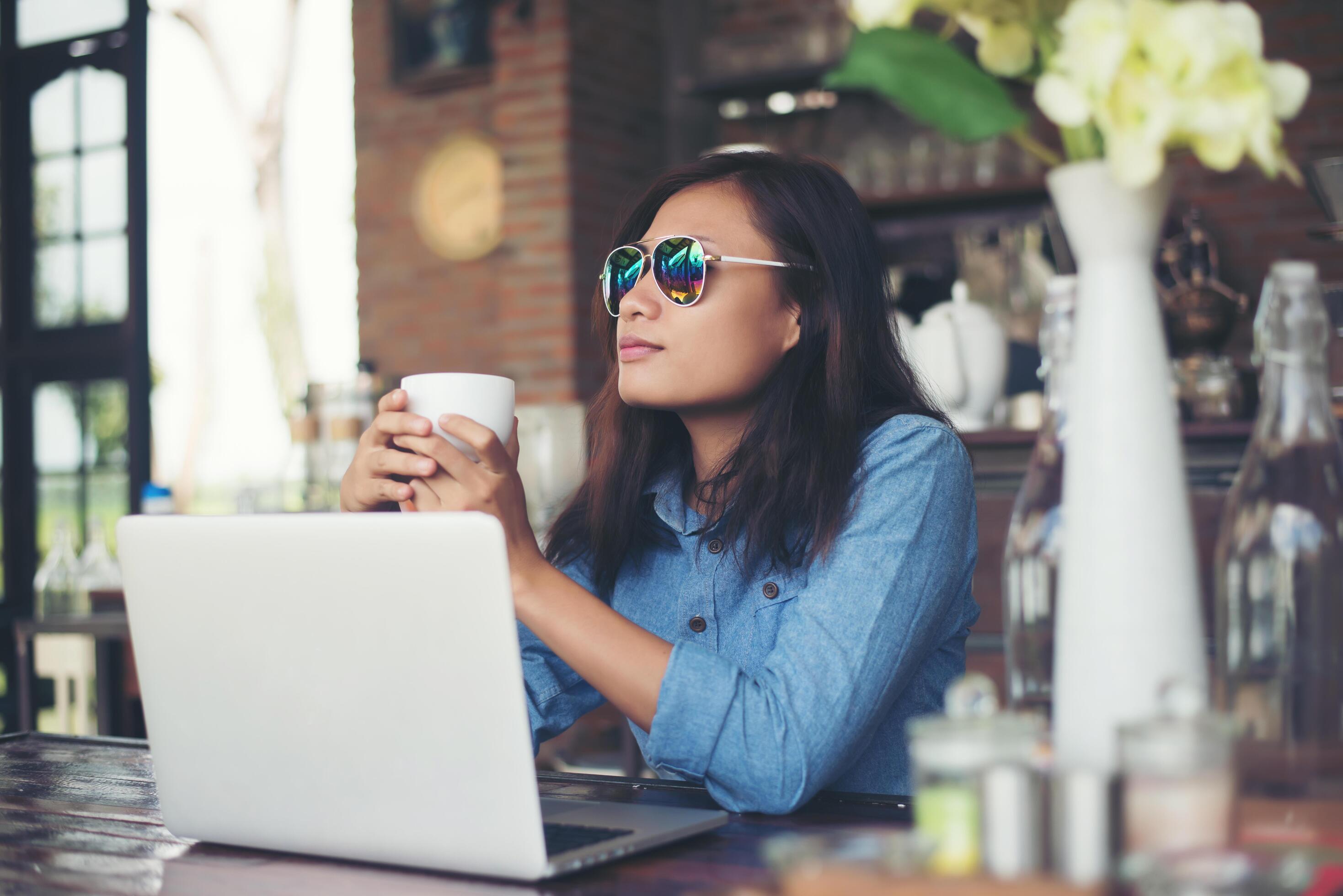 Pretty young hipster woman sitting in a cafe with her laptop, looked away and smiled happy, Relaxing with holiday, Woman lifestyle concept. Stock Free