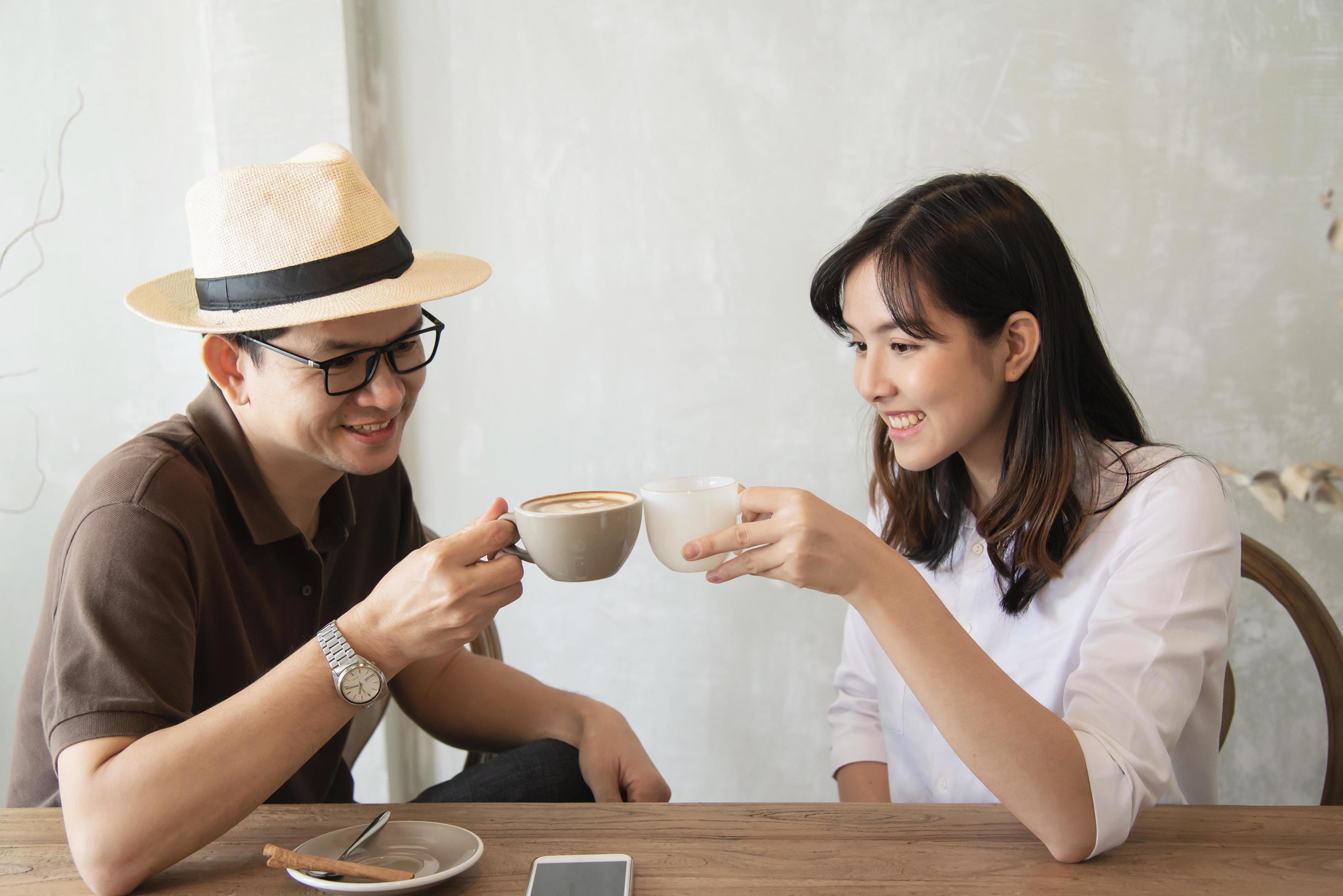 Casual man and woman talking happily while drink coffee and looking mobile phone – happy time lifestyle in coffee shop Stock Free