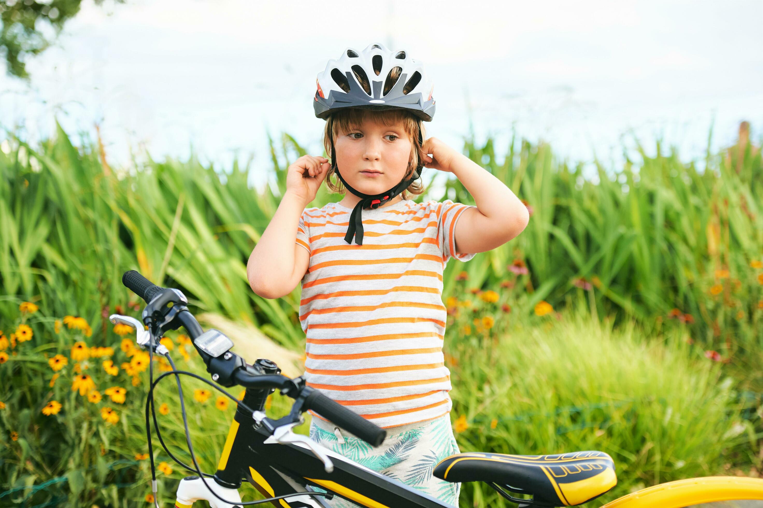 Cute little boy riding bicycle in the park, sport for children, active family outside. Child putting safe helmet Stock Free