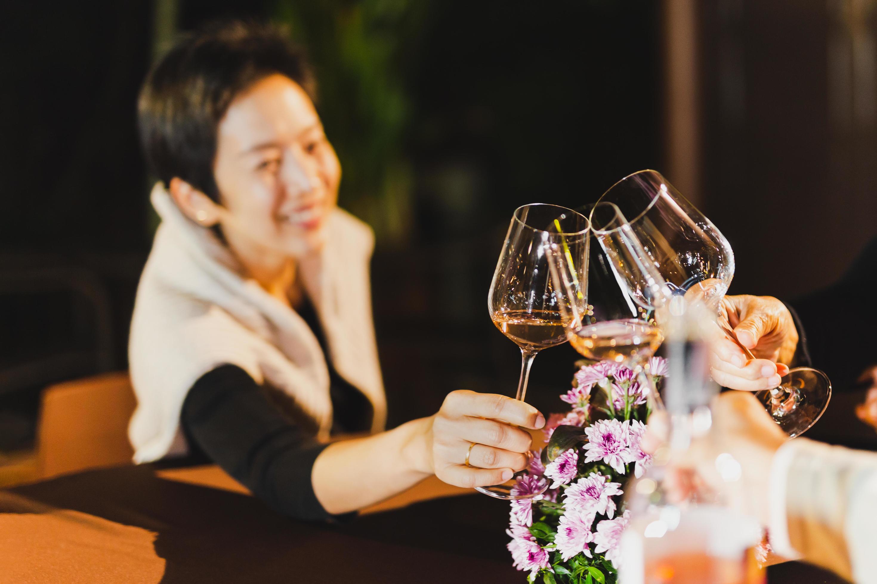 Happy woman clinking glass of wine with family sitting at dinner table. Stock Free