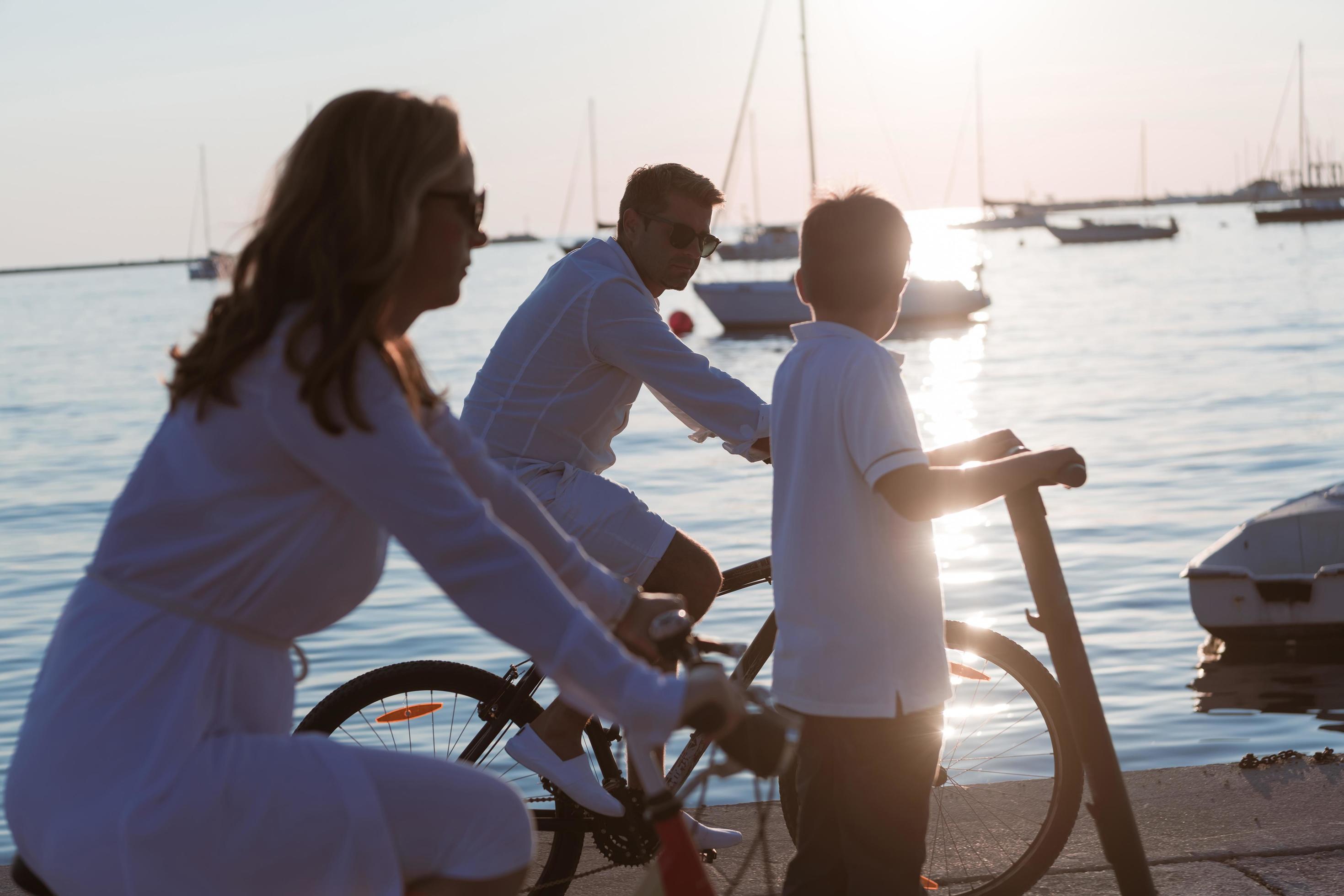 Happy family enjoying a beautiful morning by the sea together, parents riding a bike and their son riding an electric scooter. Selective focus Stock Free