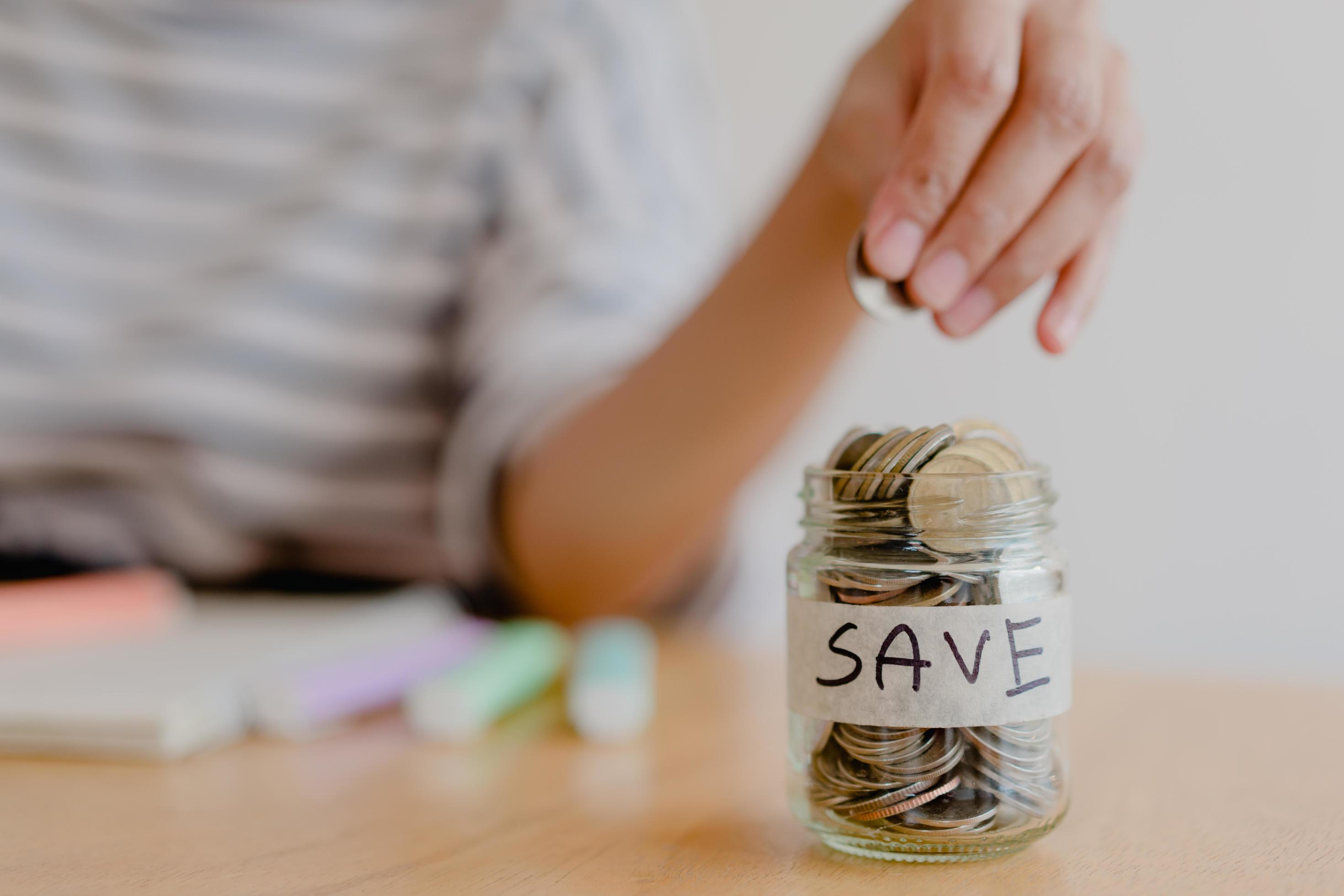 asian woman hand is putting a coin in a glass bottle on wooden table, Investment business, retirement, finance and saving money for future concept. Stock Free