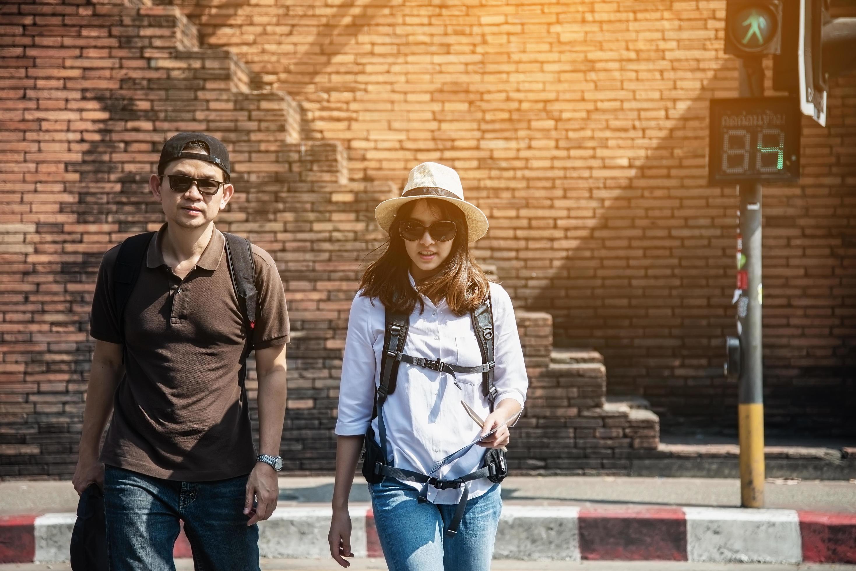 Asian backpack couple tourist holding city map crossing the road – travel people vacation lifestyle concept Stock Free