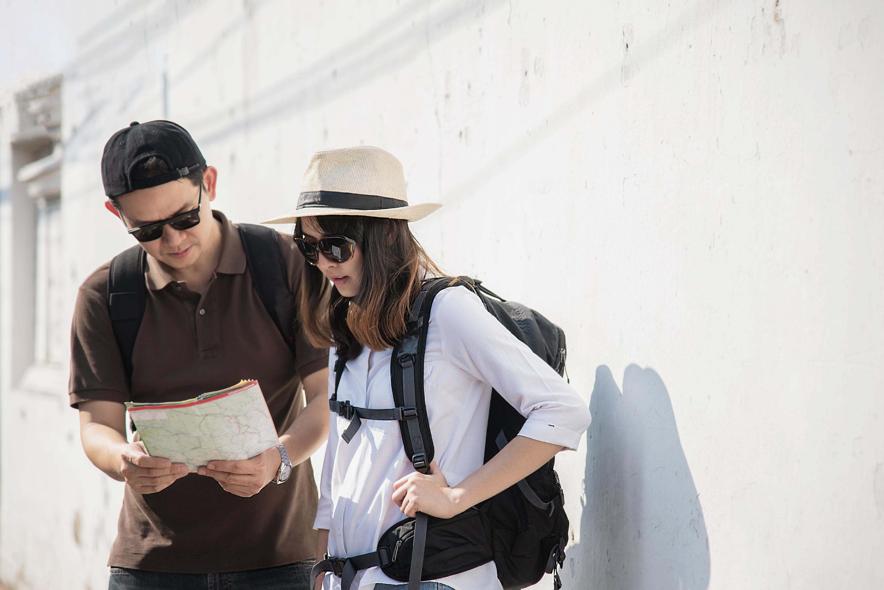 Asian backpack couple tourist holding city map crossing the road – travel people vacation lifestyle concept Stock Free