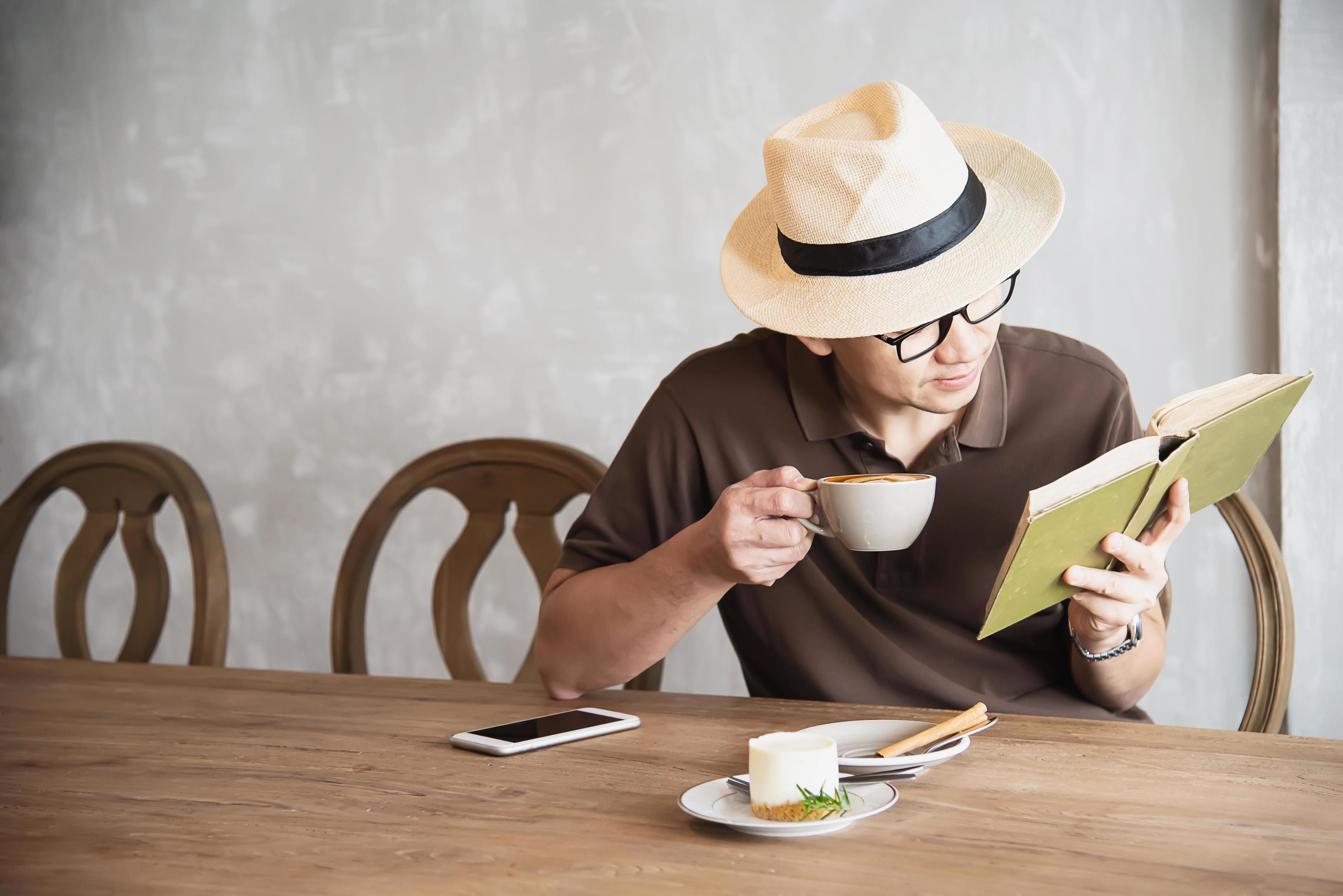 Relax Asian man drink coffee and read book in a modern style coffee shop – people with coffee cup easy lifestyle concept Stock Free