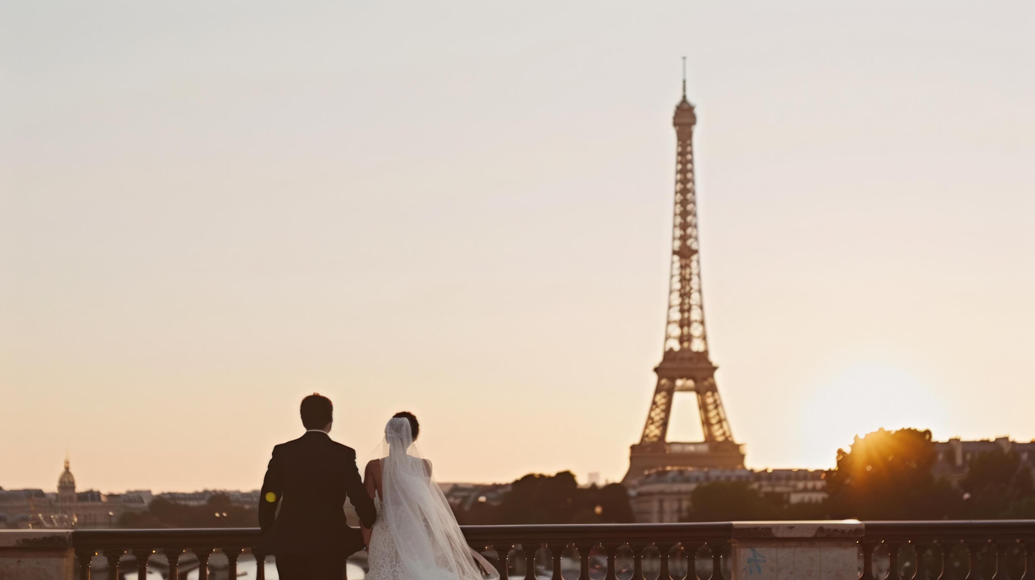 Newlywed couple in wedding attire admires the Eiffel Tower at sunset, celebrating their romantic journey in Paris. Stock Free