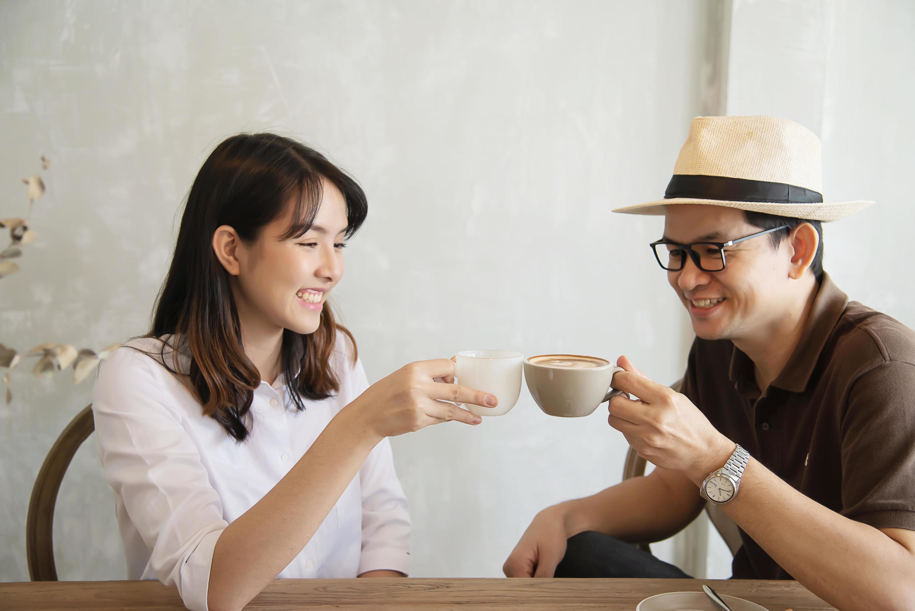 Casual man and woman talking happily while drink coffee and looking mobile phone – happy time lifestyle in coffee shop Stock Free