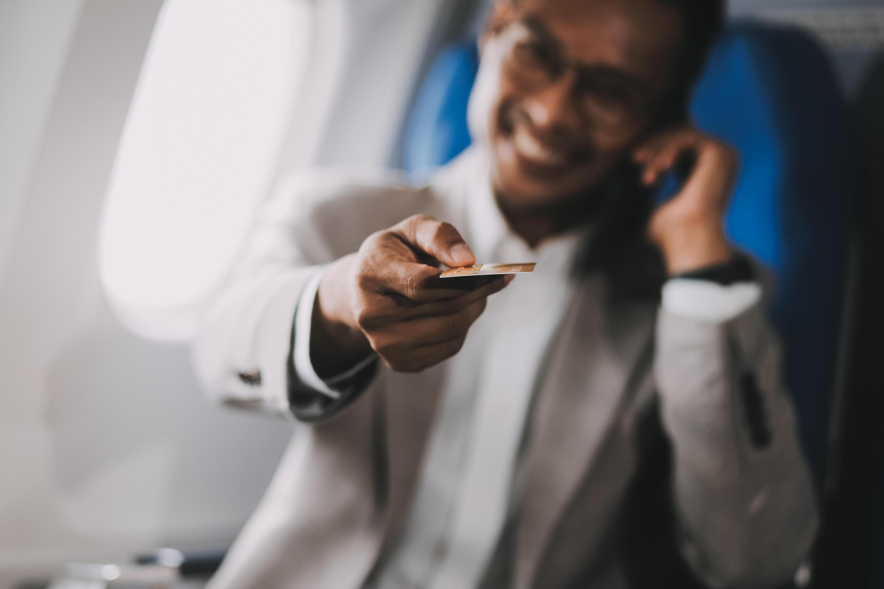 Businessman holding credit card and looking at camera near laptop in private jet Stock Free