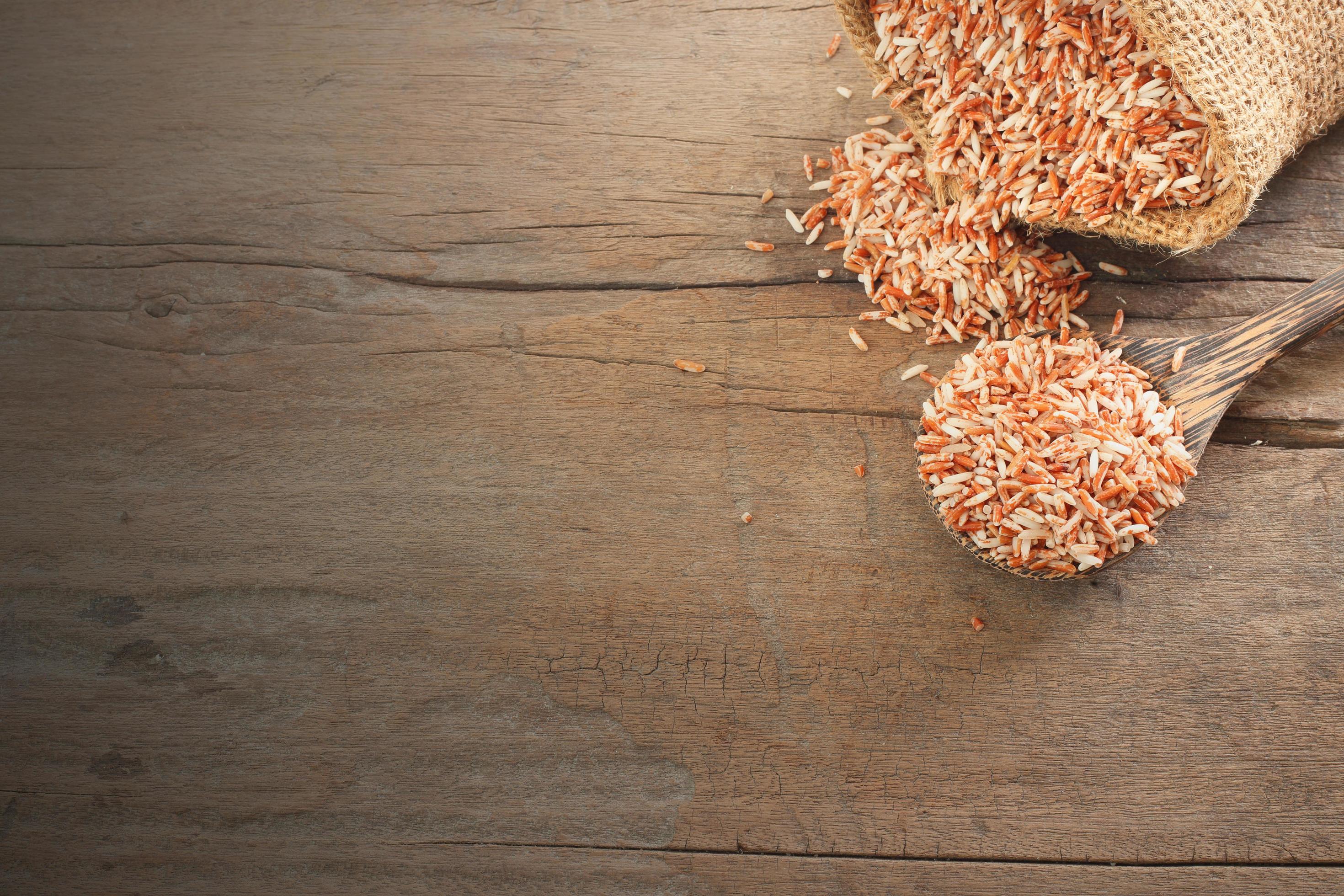 Thai cereal food – Top view of red organic rice, brown rice in wooden spoon and sack lay on wooden table with copy space Stock Free