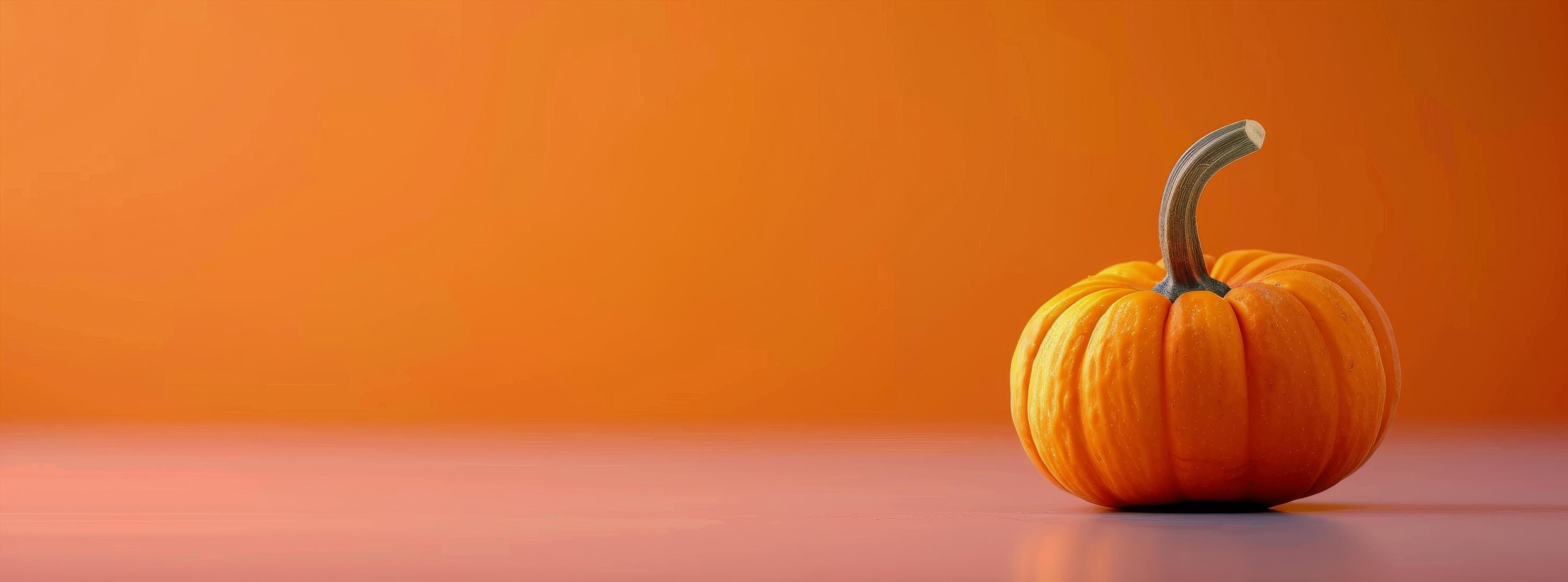 Vibrant Orange Pumpkin on White Surface Against Bright Orange Background in Autumn Stock Free