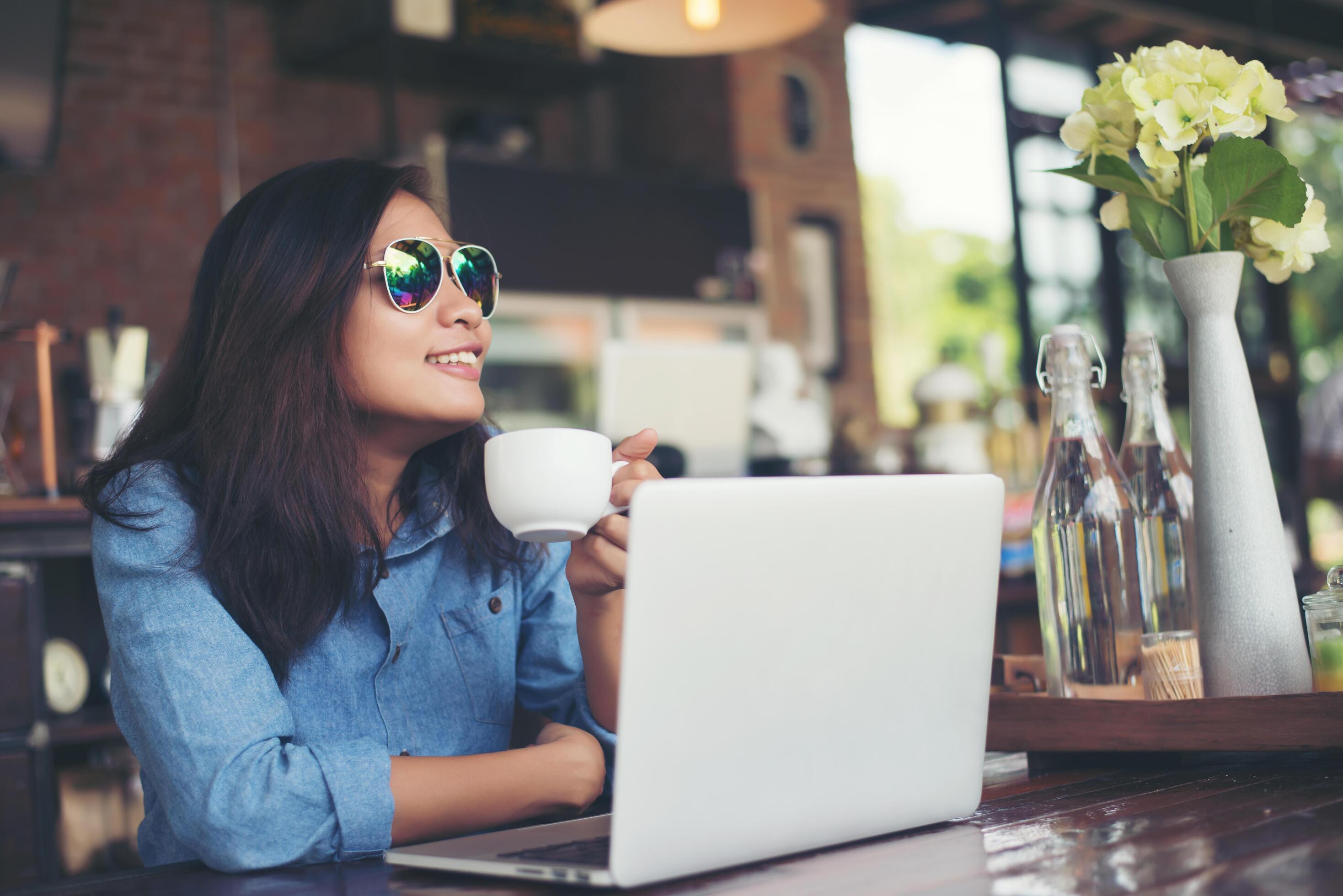 Pretty young hipster woman sitting in a cafe with her laptop, looked away and smiled happy, Relaxing with holiday, Woman lifestyle concept. Stock Free