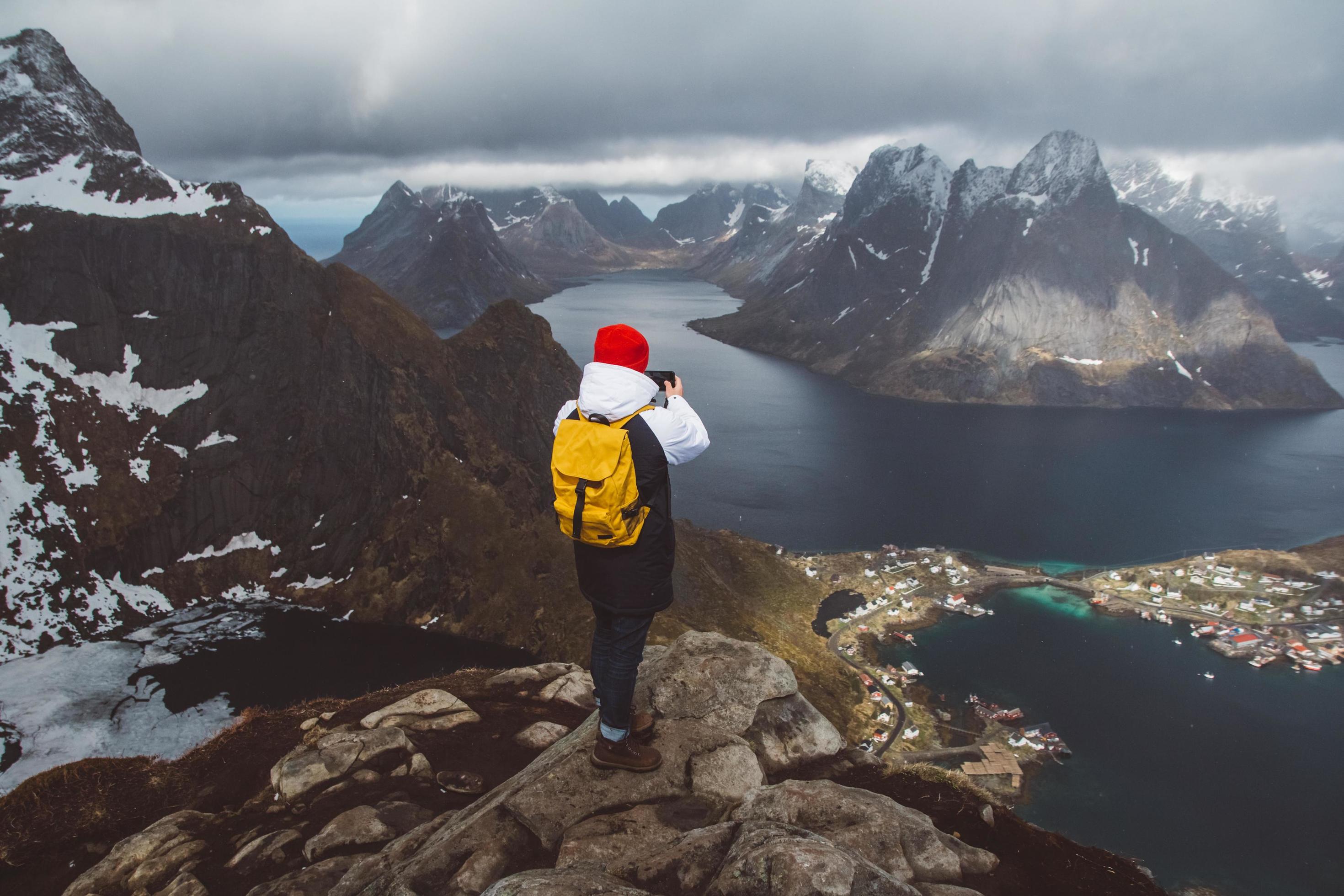 Man traveler taking photo with a smartphone hiking on Reinebringen mountain ridge in Norway lifestyle adventure traveling Stock Free