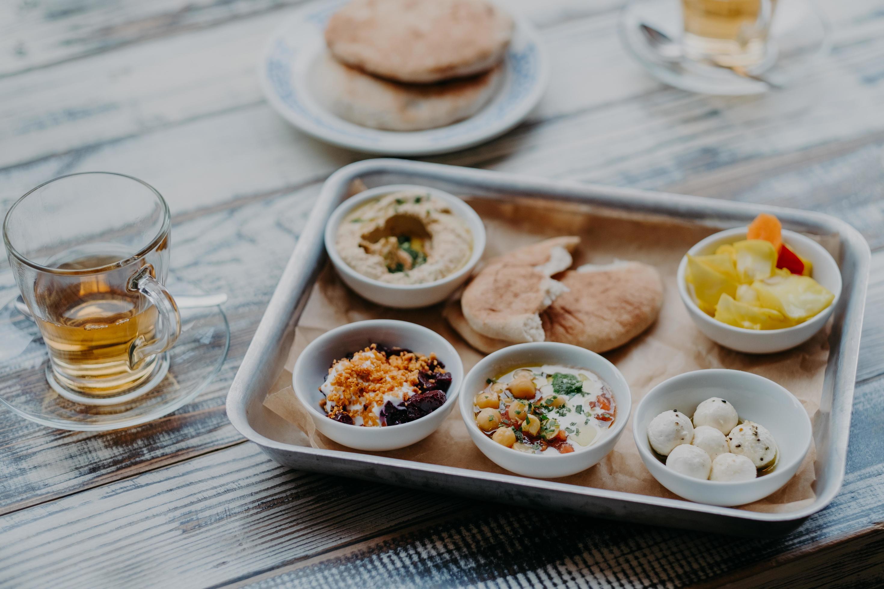 Overhead image of traditional Israel food on tray. Hummus, domestic goat cheese, tomatoe core, beetroot with spices, pita bread, beverage in glass Stock Free