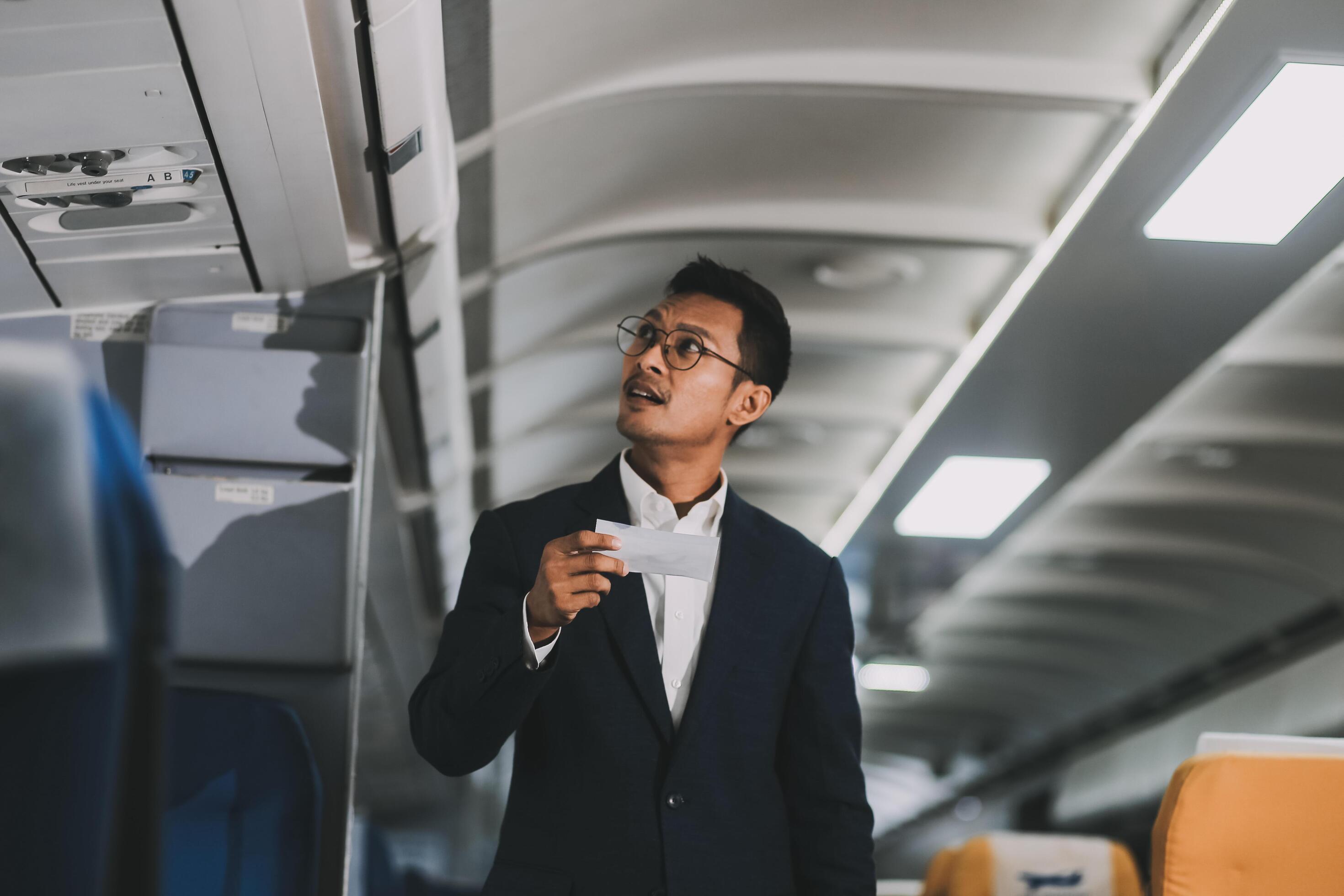 Handsome Asian male passenger takes his carry-on luggage out of the overhead locker after landing at his destination. transportation concept Stock Free