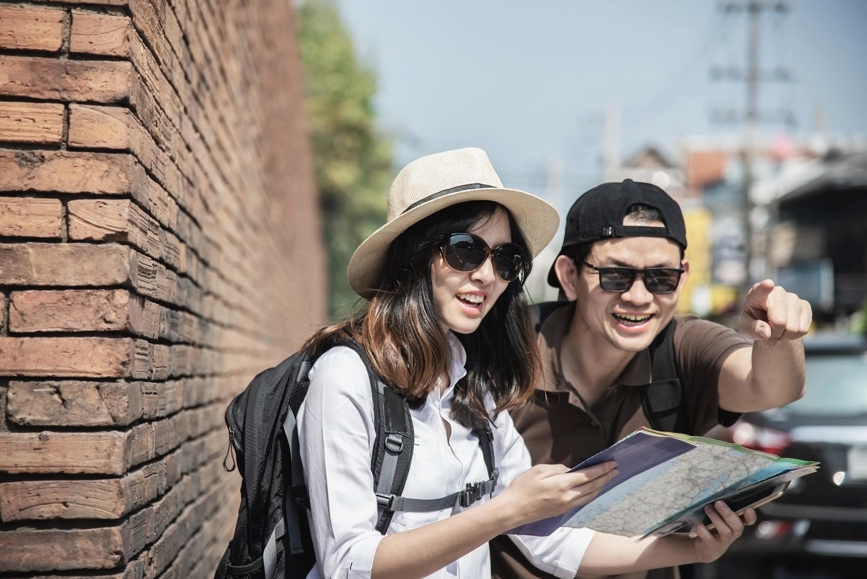 Asian backpack couple tourist holding city map crossing the road – travel people vacation lifestyle concept Stock Free