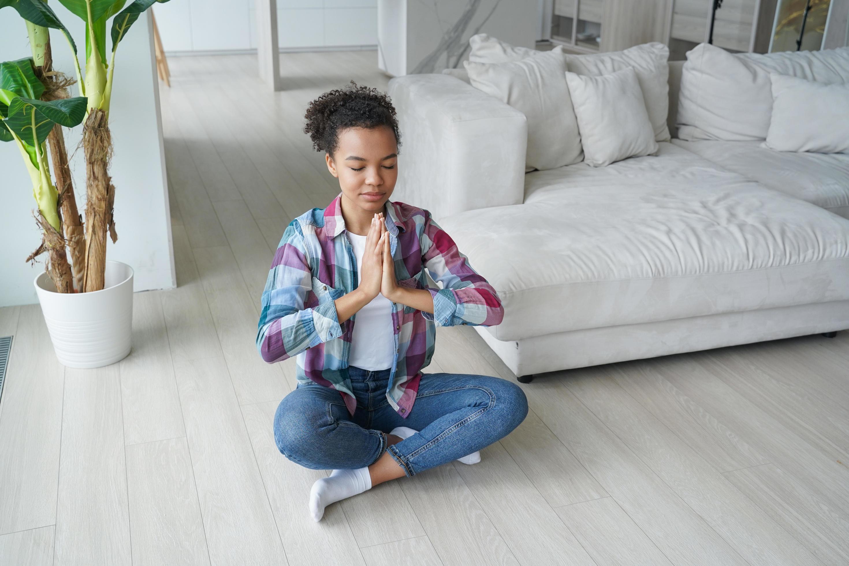 Calm mixed race girl practicing yoga in lotus pose on floor at home. Healthy lifestyle, meditation Stock Free