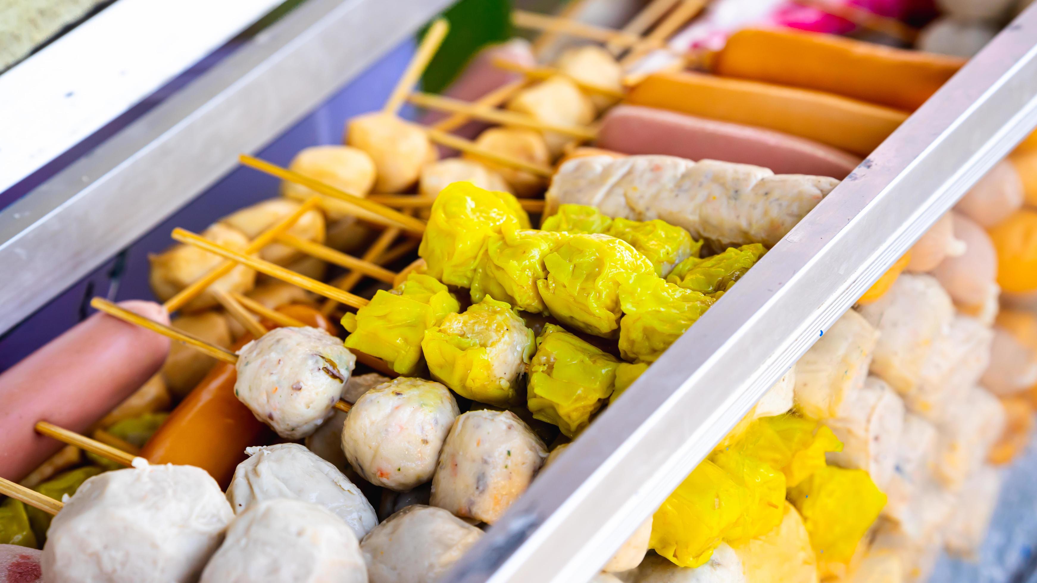 Assorted meatballs and sausage skewers are lined up in glass with ice for sale. Street Food. Stock Free