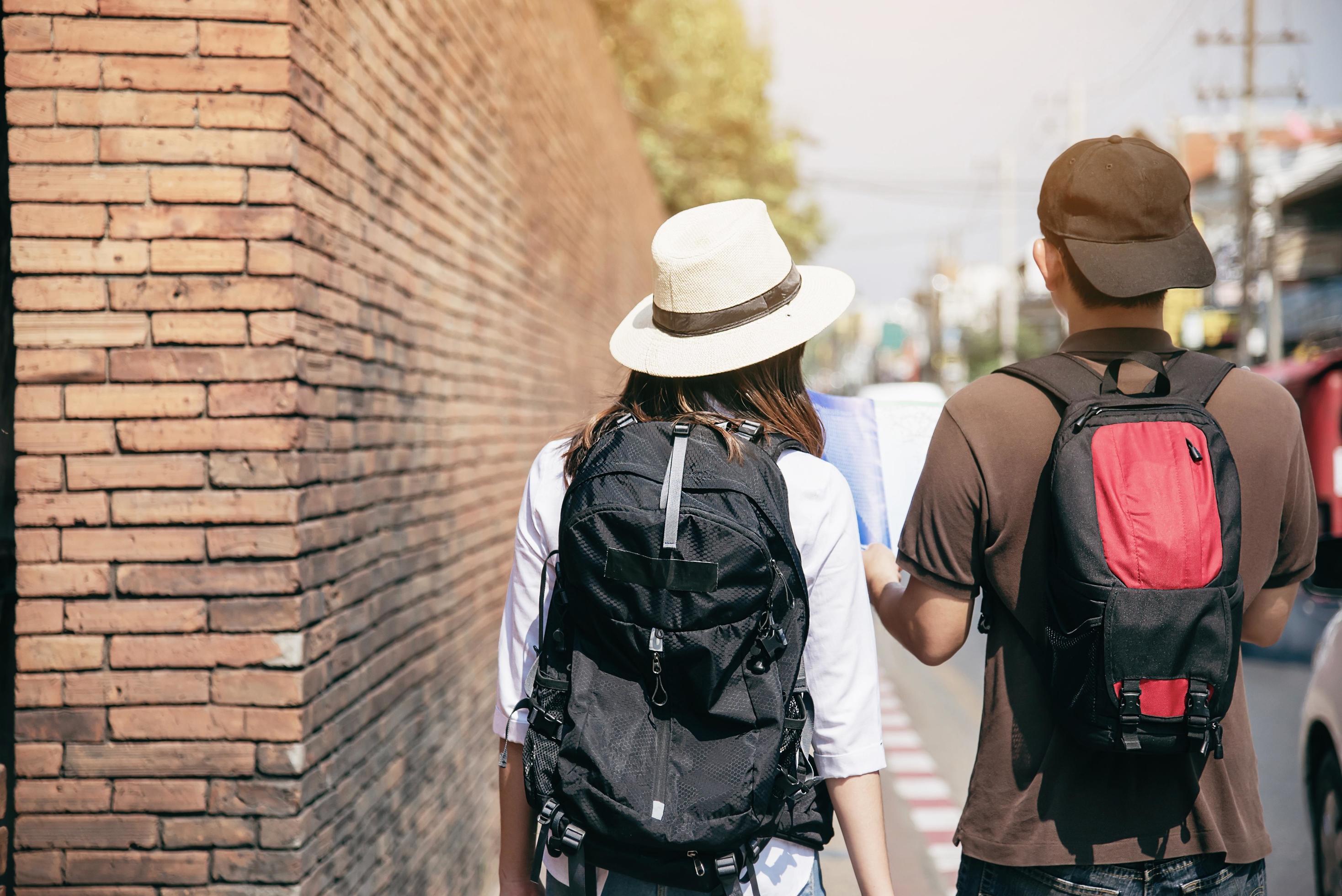 Asian backpack couple tourist holding city map crossing the road – travel people vacation lifestyle concept Stock Free