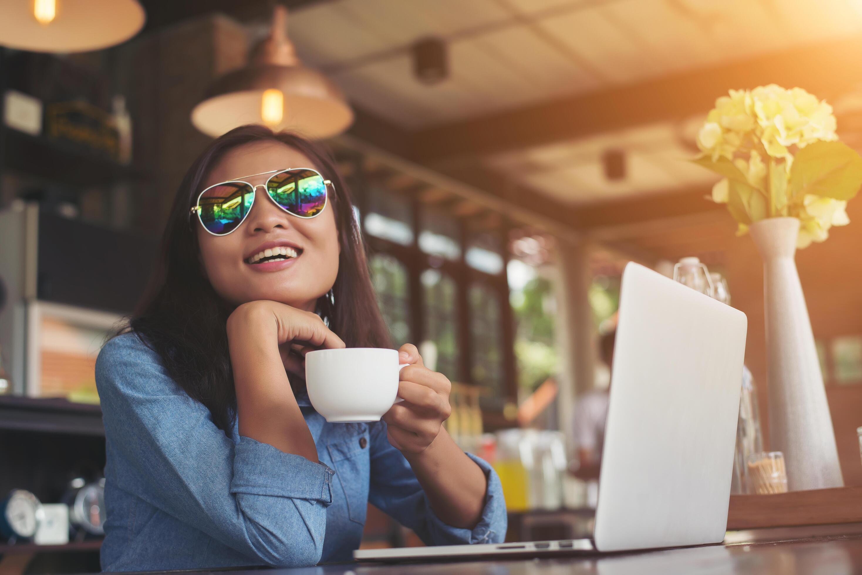 Pretty young hipster woman sitting in a cafe with her laptop, looked away and smiled happy, Relaxing with holiday, Woman lifestyle concept. Stock Free