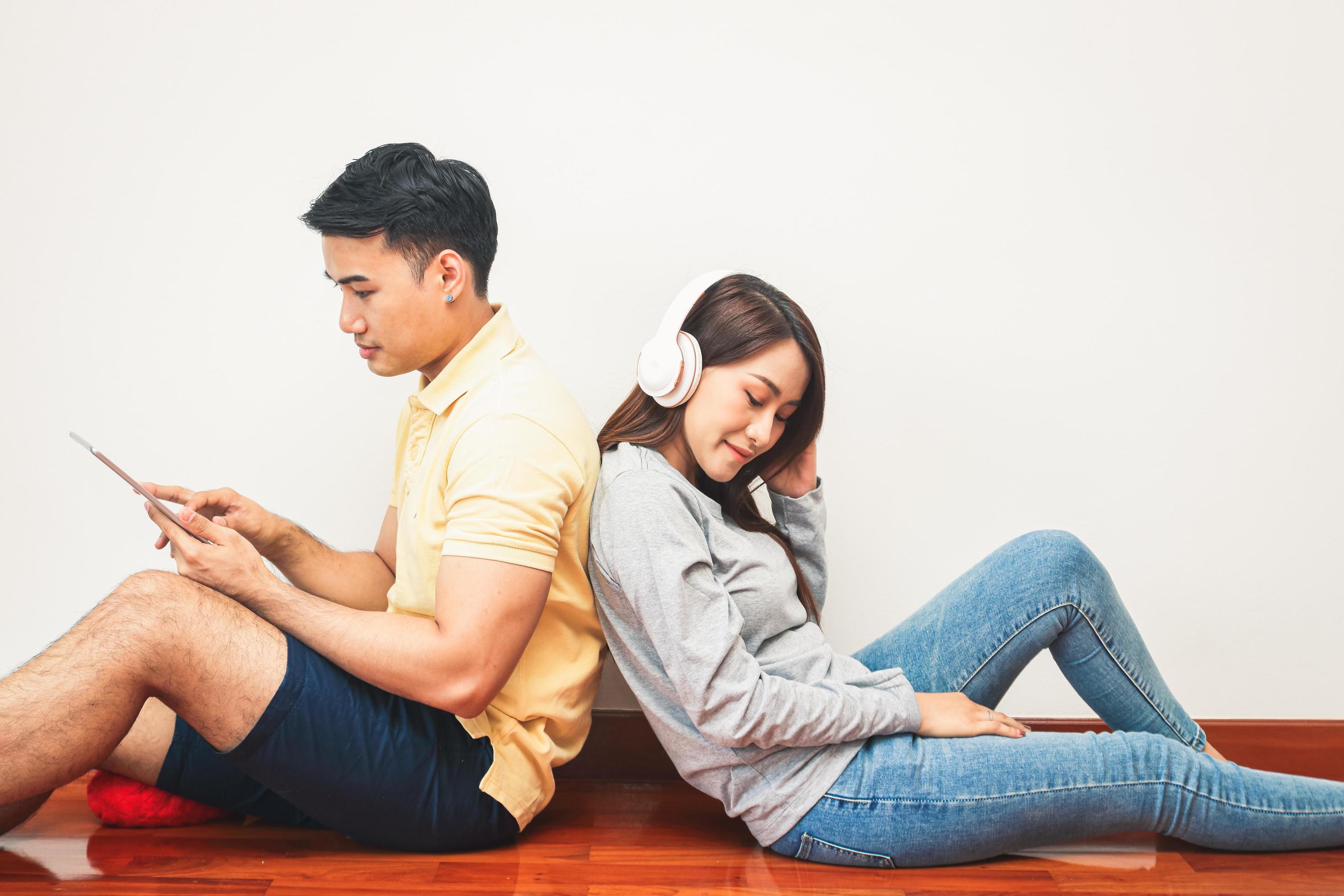 Asian couples sit back against each other, listen to music, and play the tablet. Happy to live together in his own home. Modern family concept Stock Free