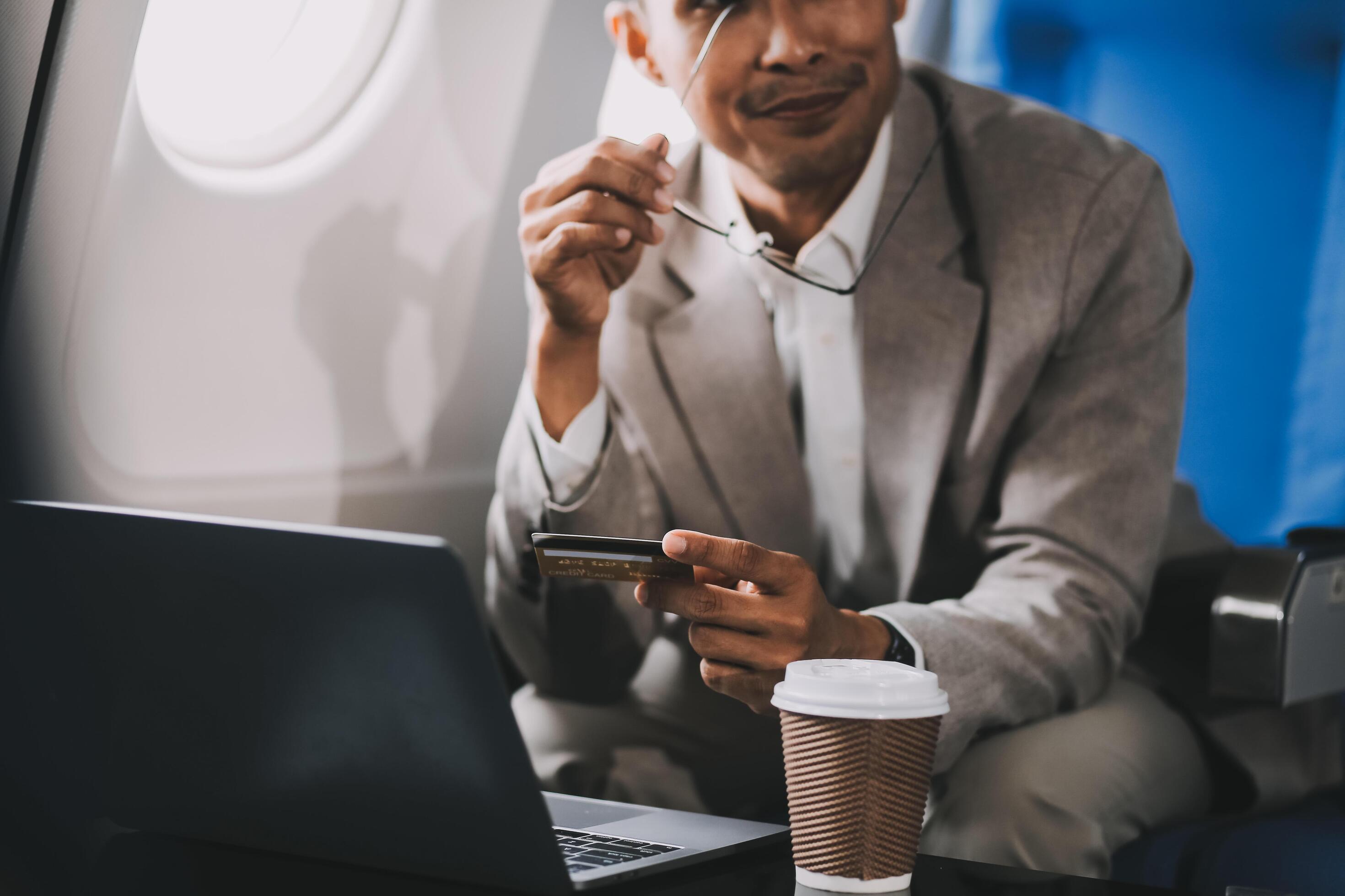 Businessman holding credit card and looking at camera near laptop in private jet Stock Free