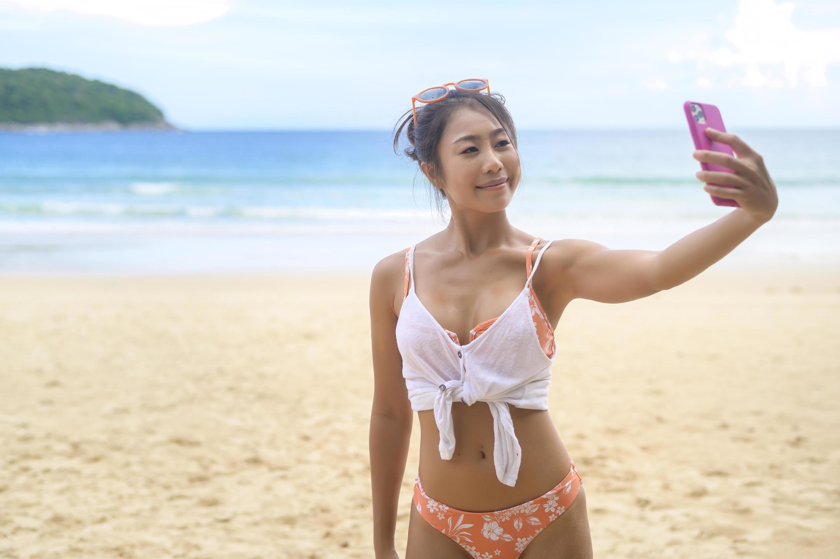 Young Beautiful woman in Bikini listening to music and using smartphone on the beach, Summer, vacation, holidays, Lifestyles concept. Stock Free