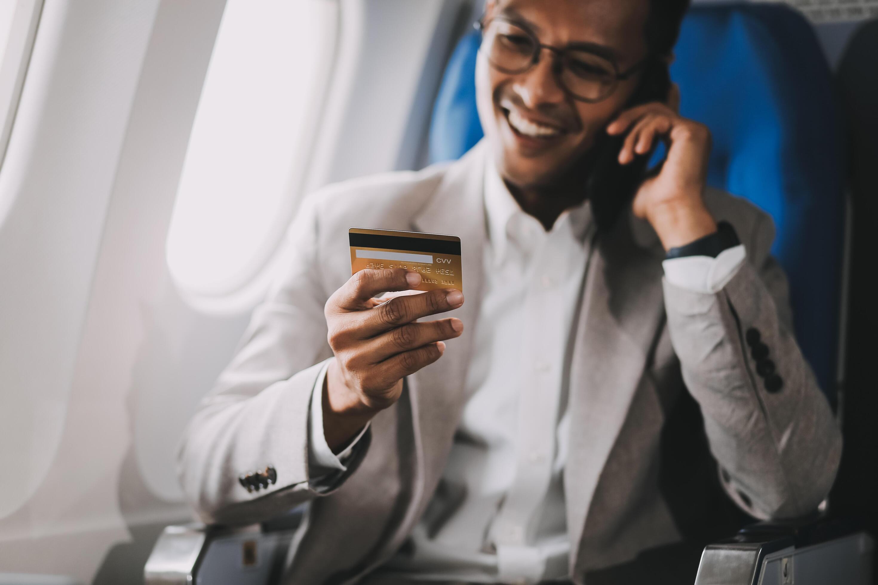 Businessman holding credit card and looking at camera near laptop in private jet Stock Free