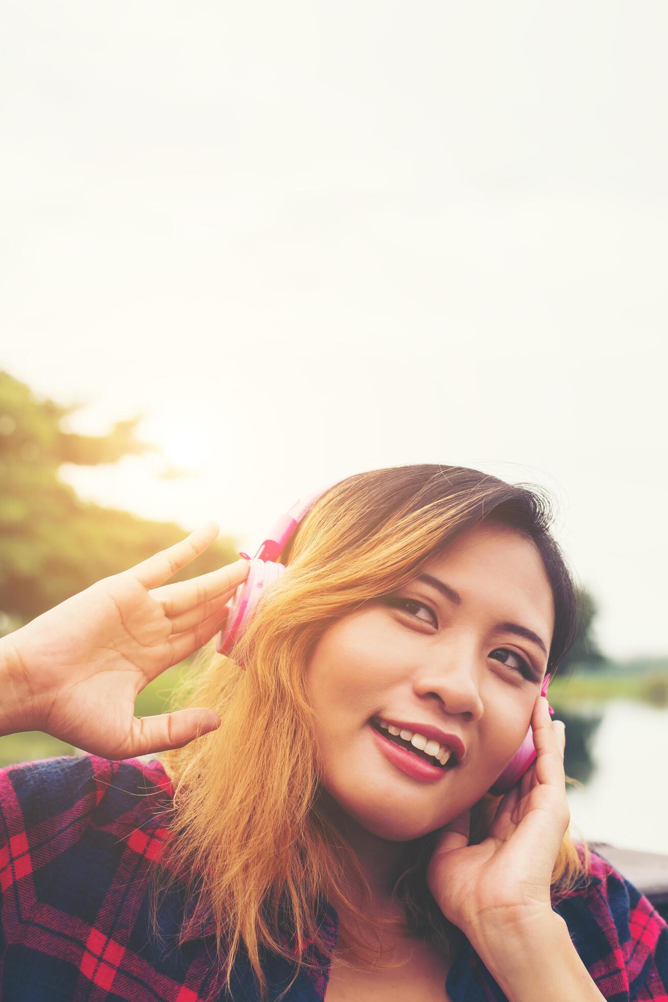 Portrait of young hipster woman with headphones sitting on pier and listening music relaxing with sunset,Lifestyle concept. Stock Free