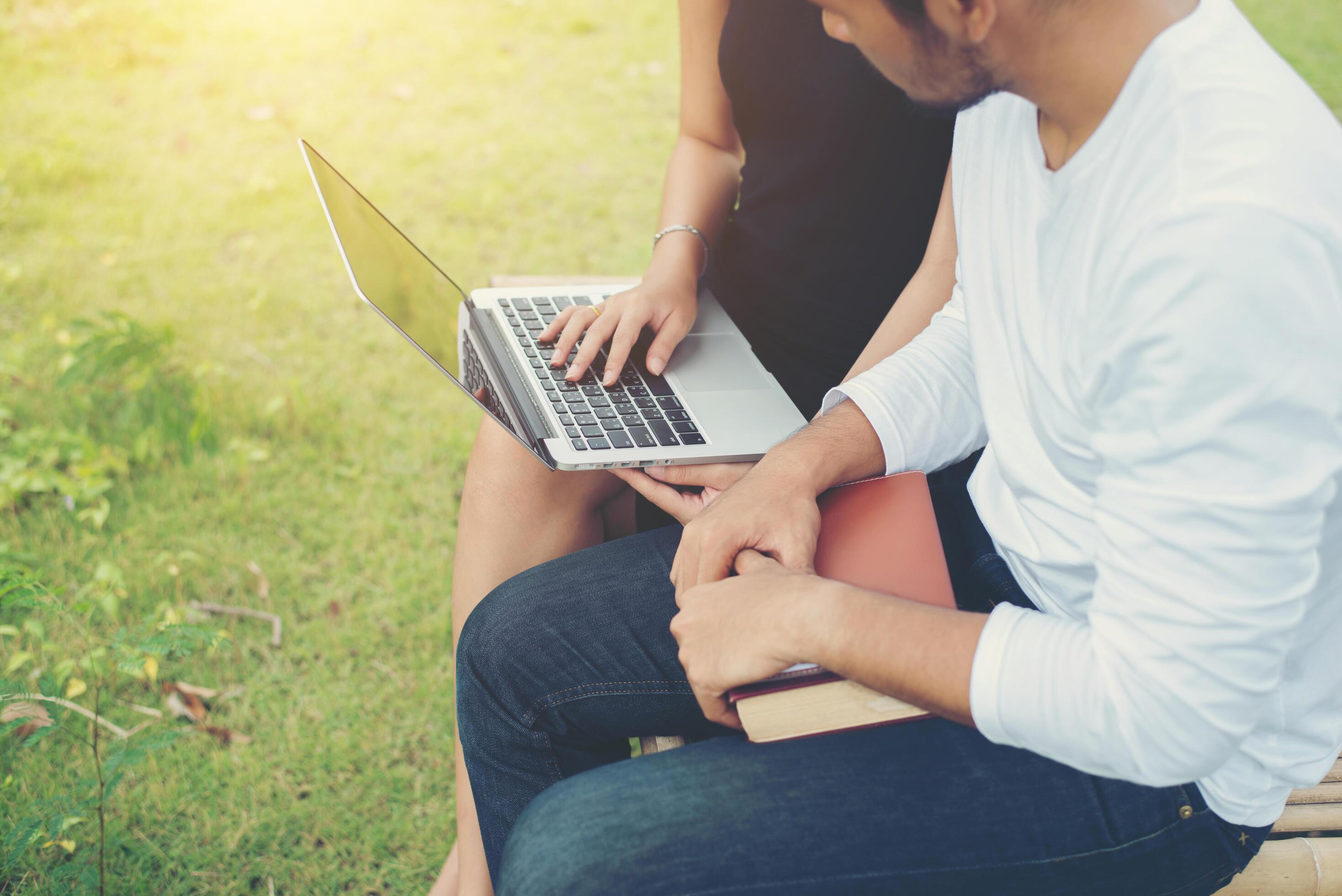 Young education couple sitting on the bench in the outdoors and good weather. And they’re happy, Lifestyle concept. Stock Free