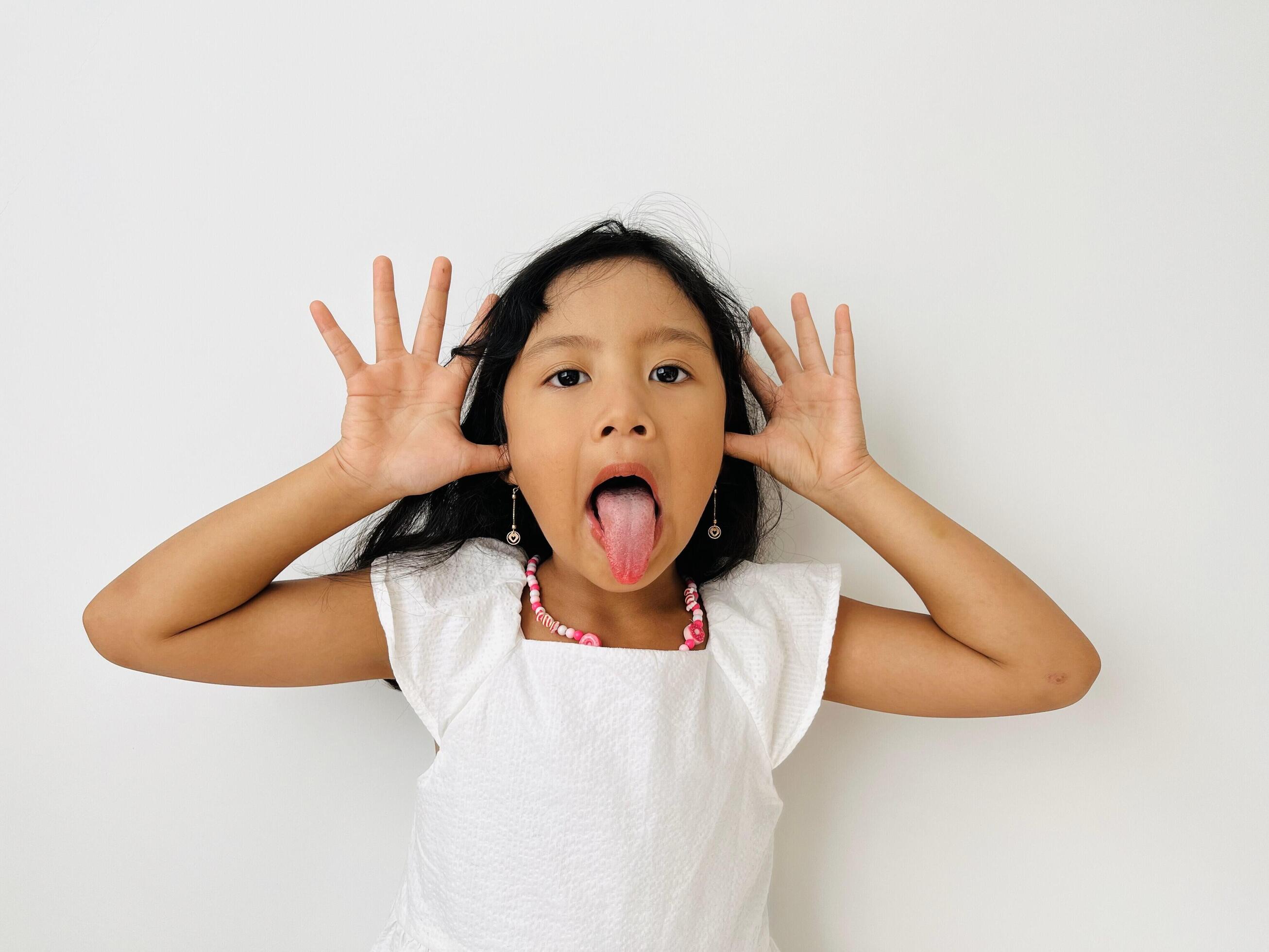 Funny Asian child girl shows tongue white background. Emotions on kid face. Happy childhood concept Stock Free