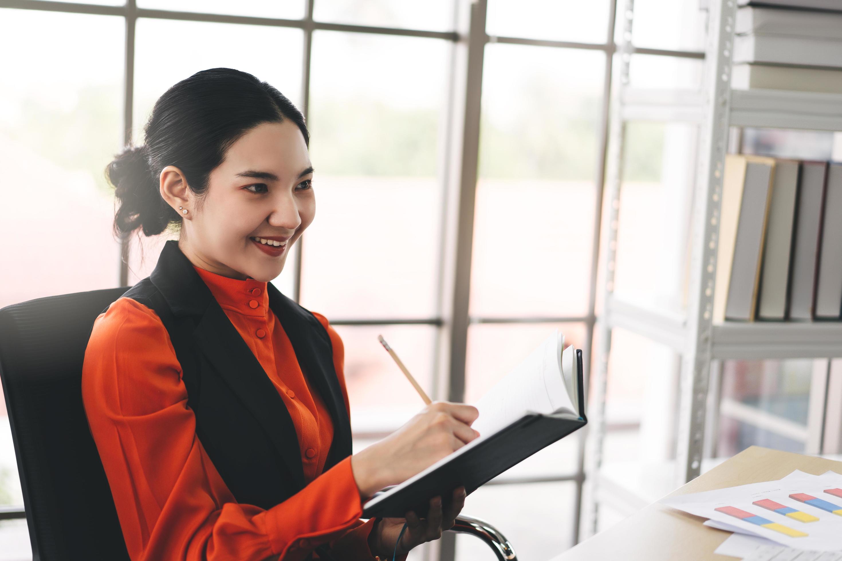 Young adult asian business woman writing on diary book at office on day Stock Free