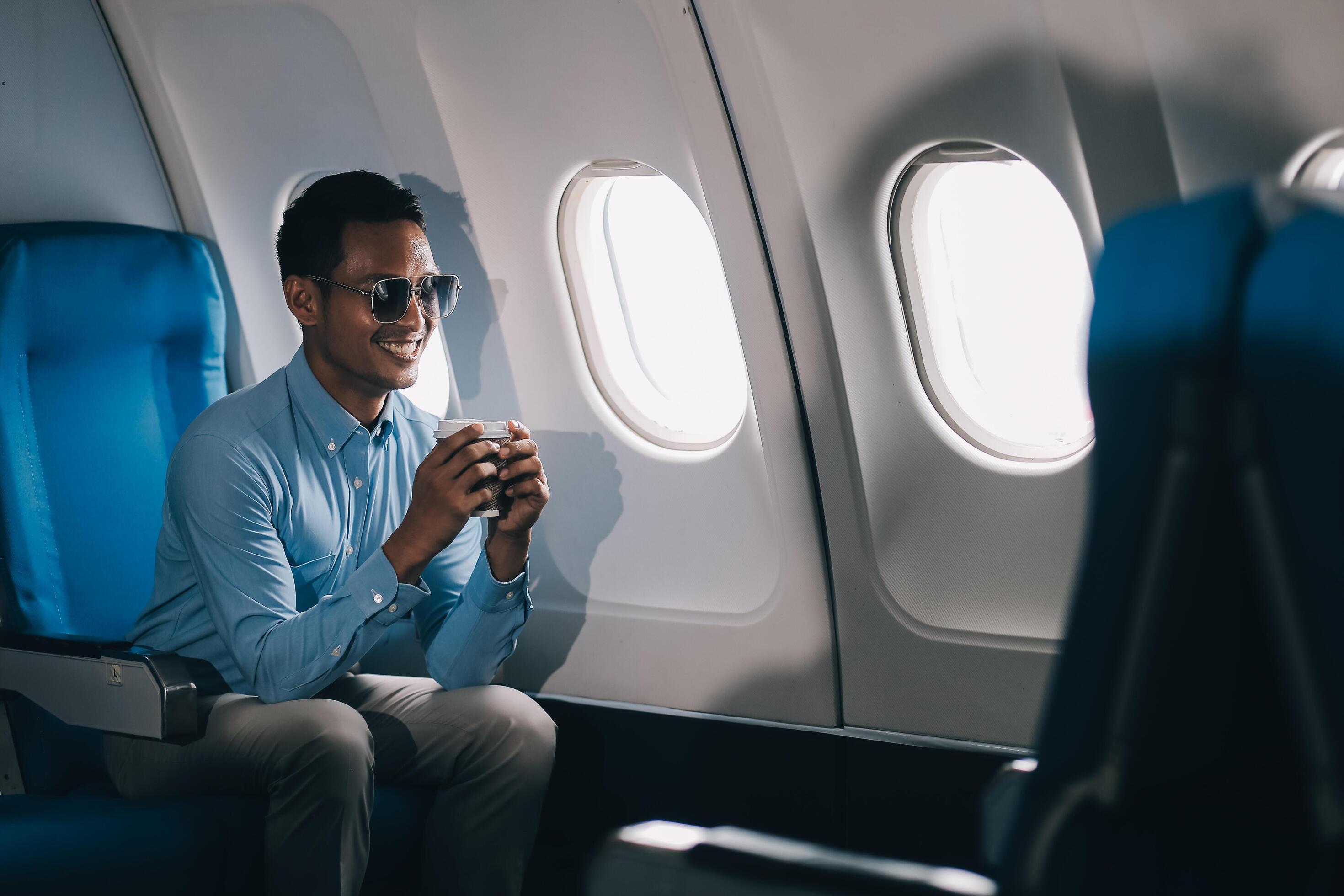 Asian businessman enjoying enjoys a coffee comfortable flight while sitting in the airplane cabin, Passengers near the window. Stock Free