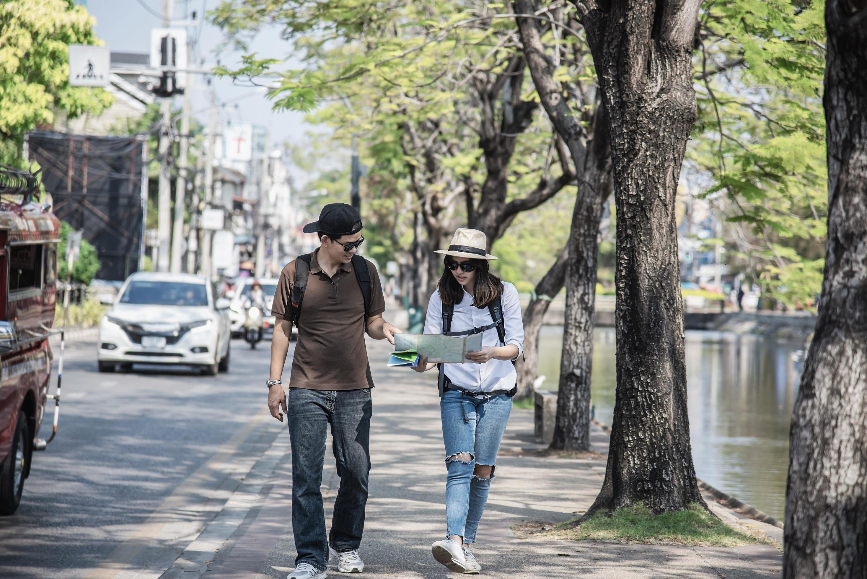 Asian backpack couple tourist holding city map crossing the road – travel people vacation lifestyle concept Stock Free