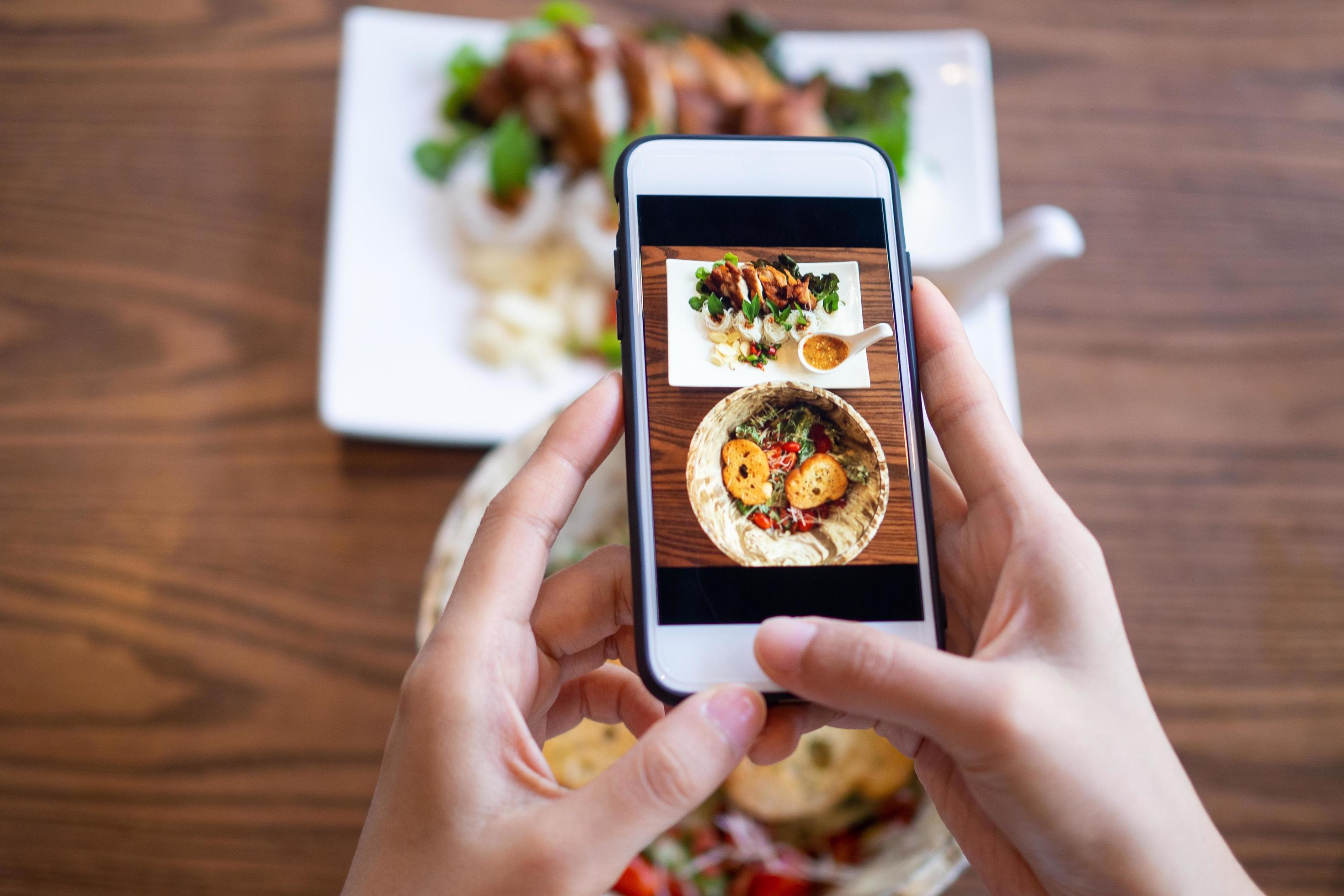 Woman using mobile phone to take pictures of food on the table. Taken on mobile and put on social networks. Stock Free