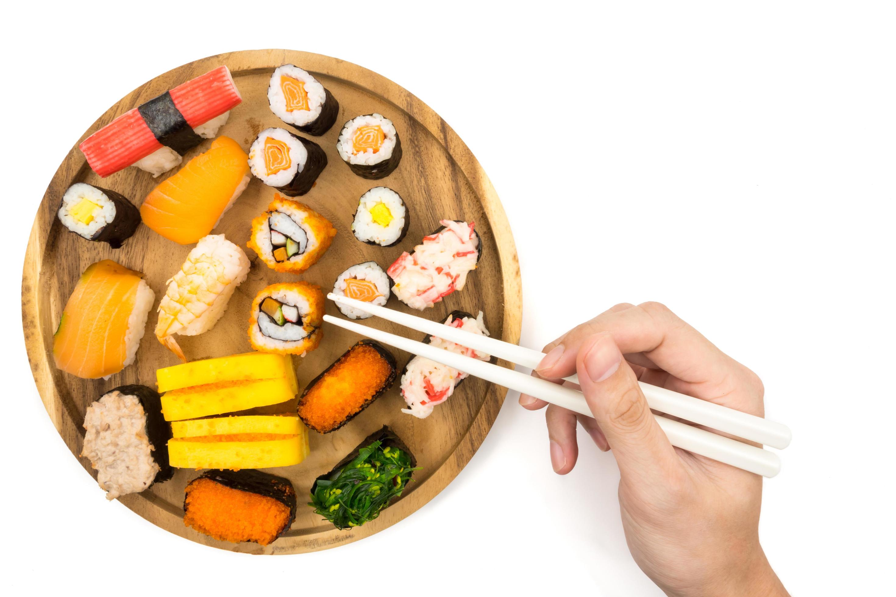 Top view of Sushi set on wooden plate and hand holding chopsticks on white background, Japanese food. Stock Free