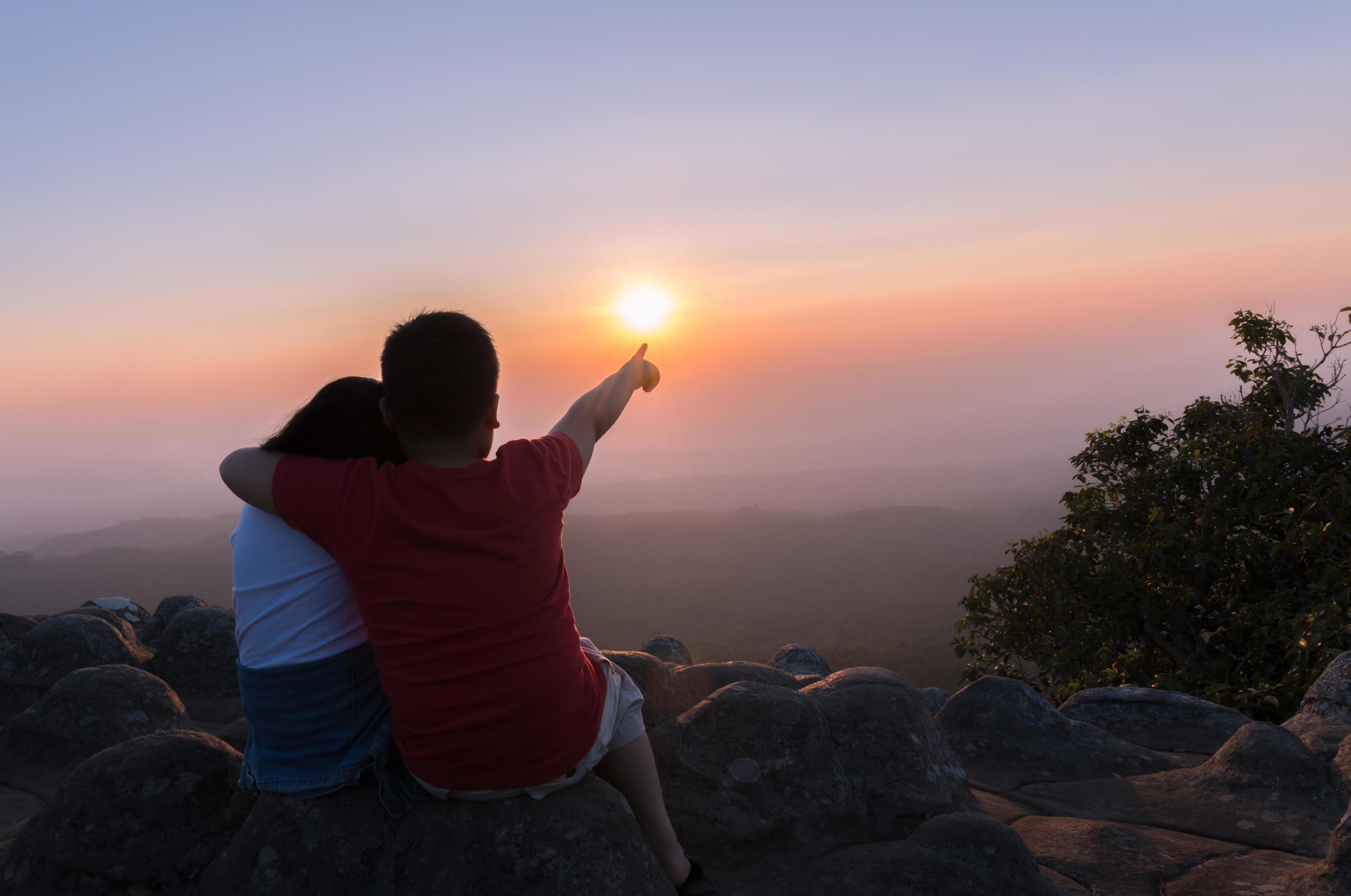 brother and sister sitting on rock and see sunset together Stock Free