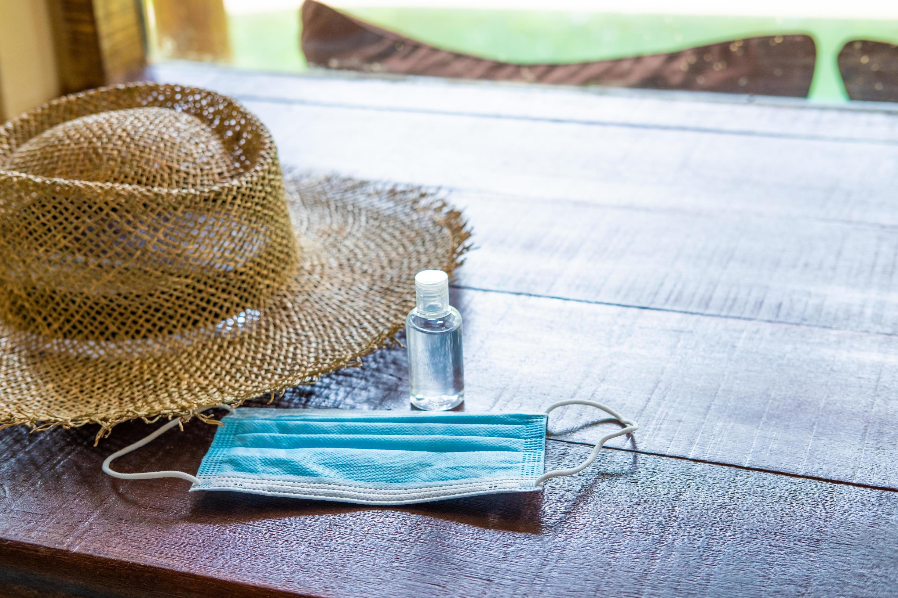 shot of surgical face mask, together with straw hat and on wooden table inside of the hotel. New normal lifestyle for traveler after Coronavirus. Stock Free