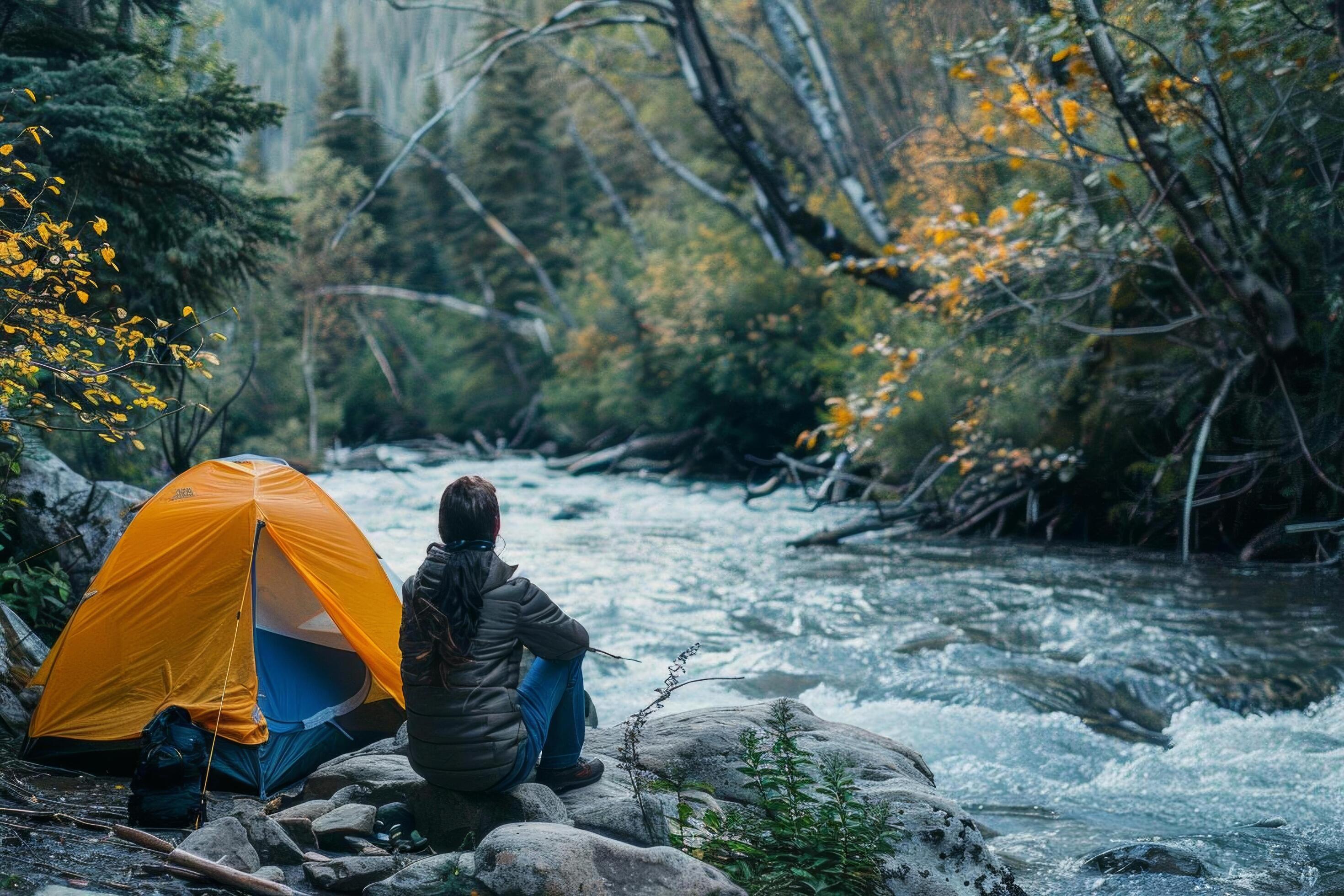 A couple enjoying a peaceful moment by their tent, with a river flowing nearby Stock Free